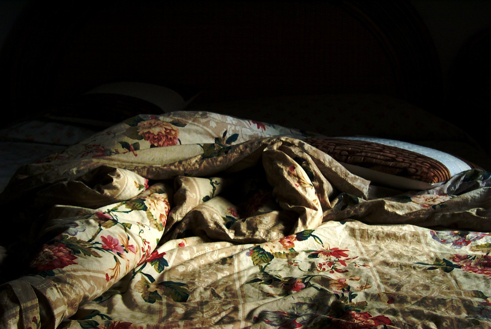an unmade bed with a flowered comforter next to a pillow