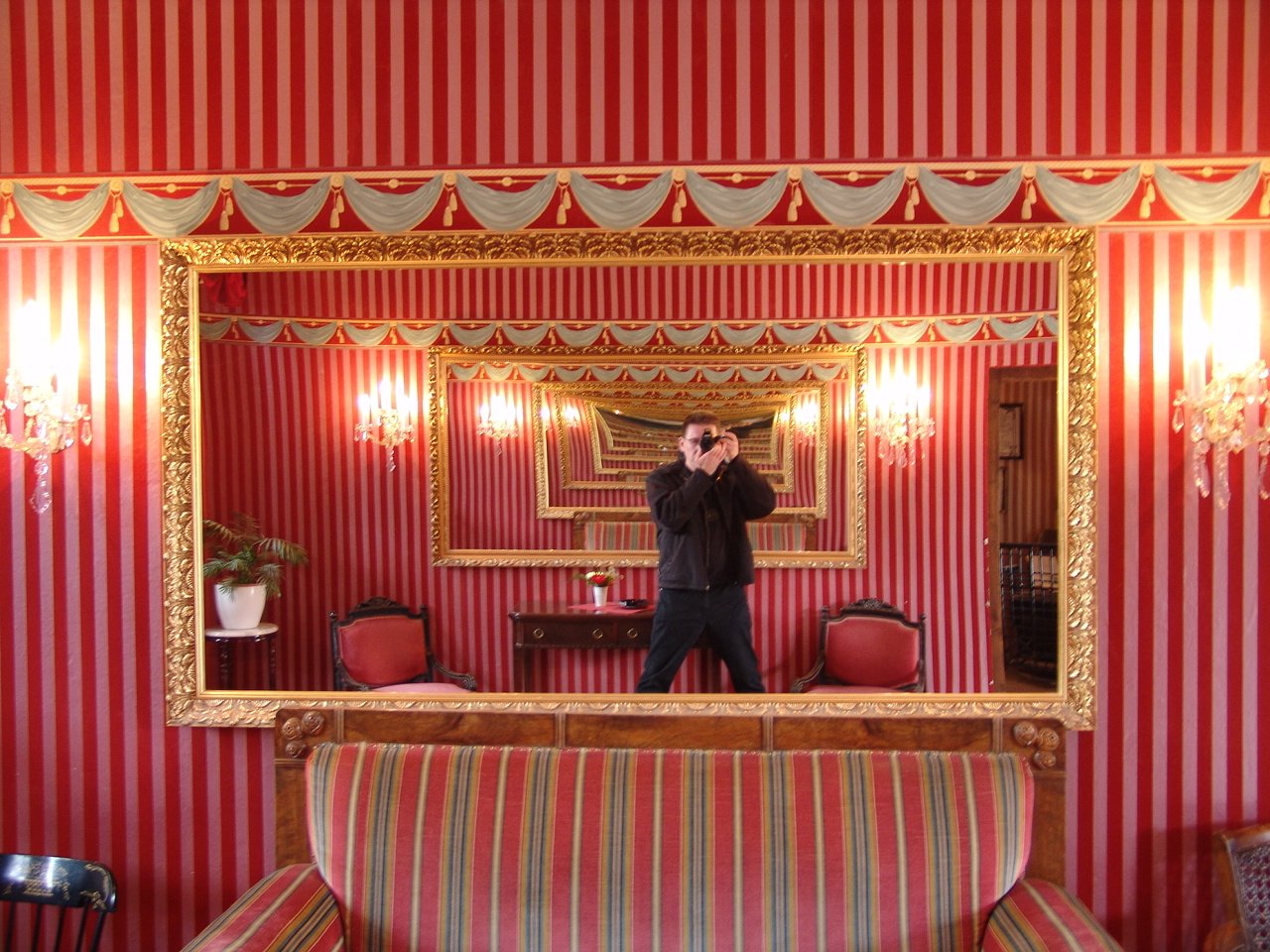 man taking pictures in large ornately decorated mirror