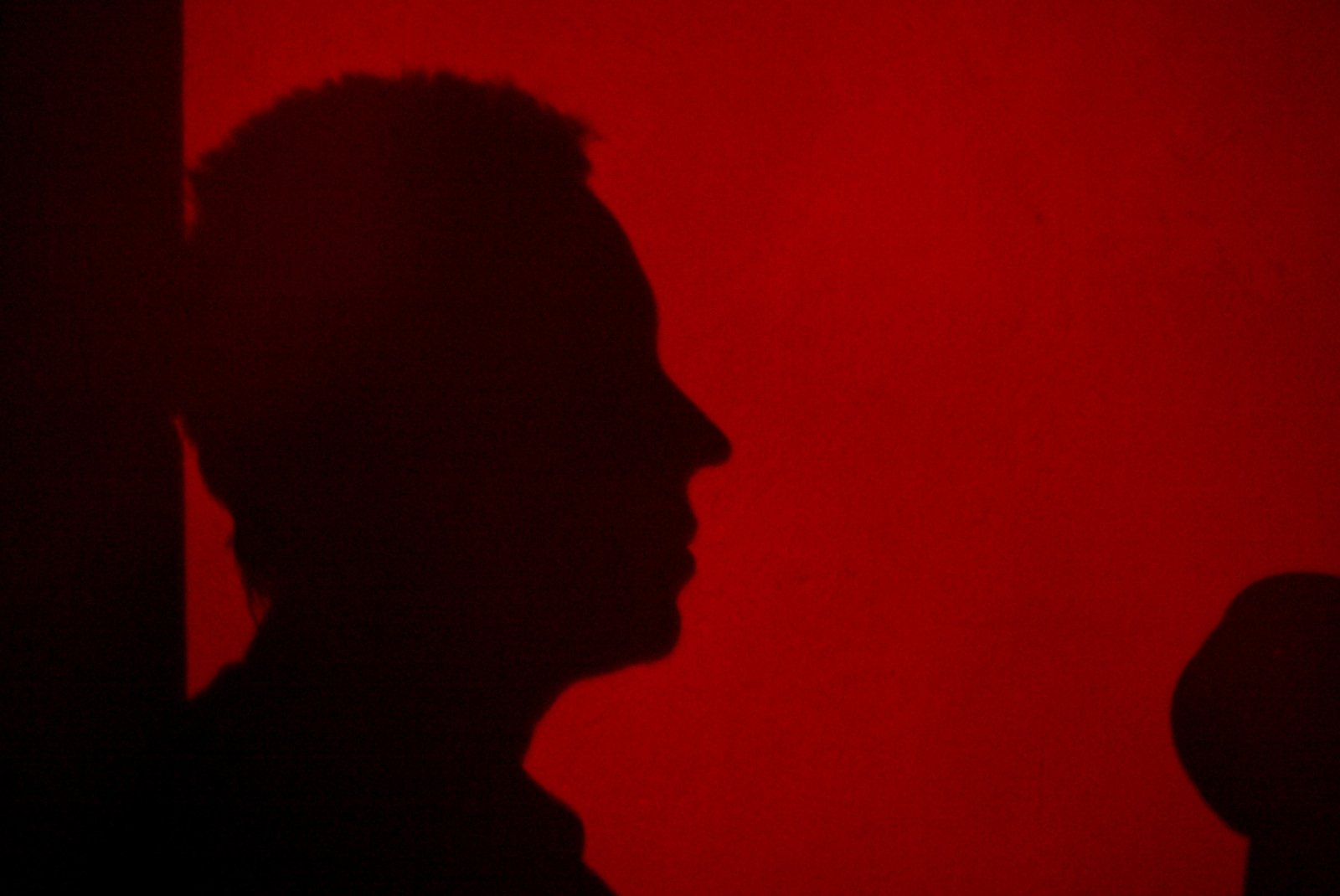 a man with shadow against a red wall with a microphone