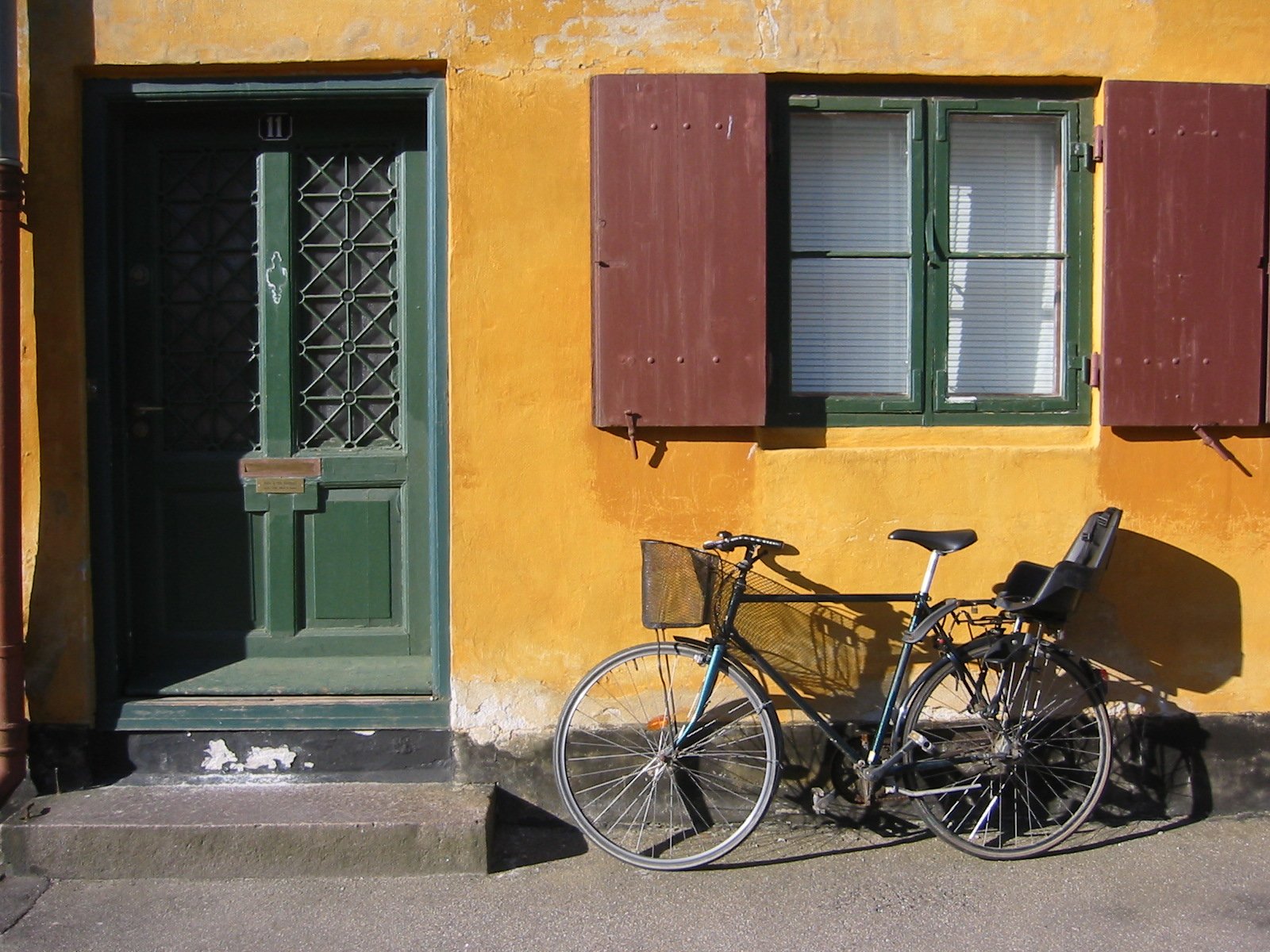 a bicycle parked in front of a yellow building with green shutters