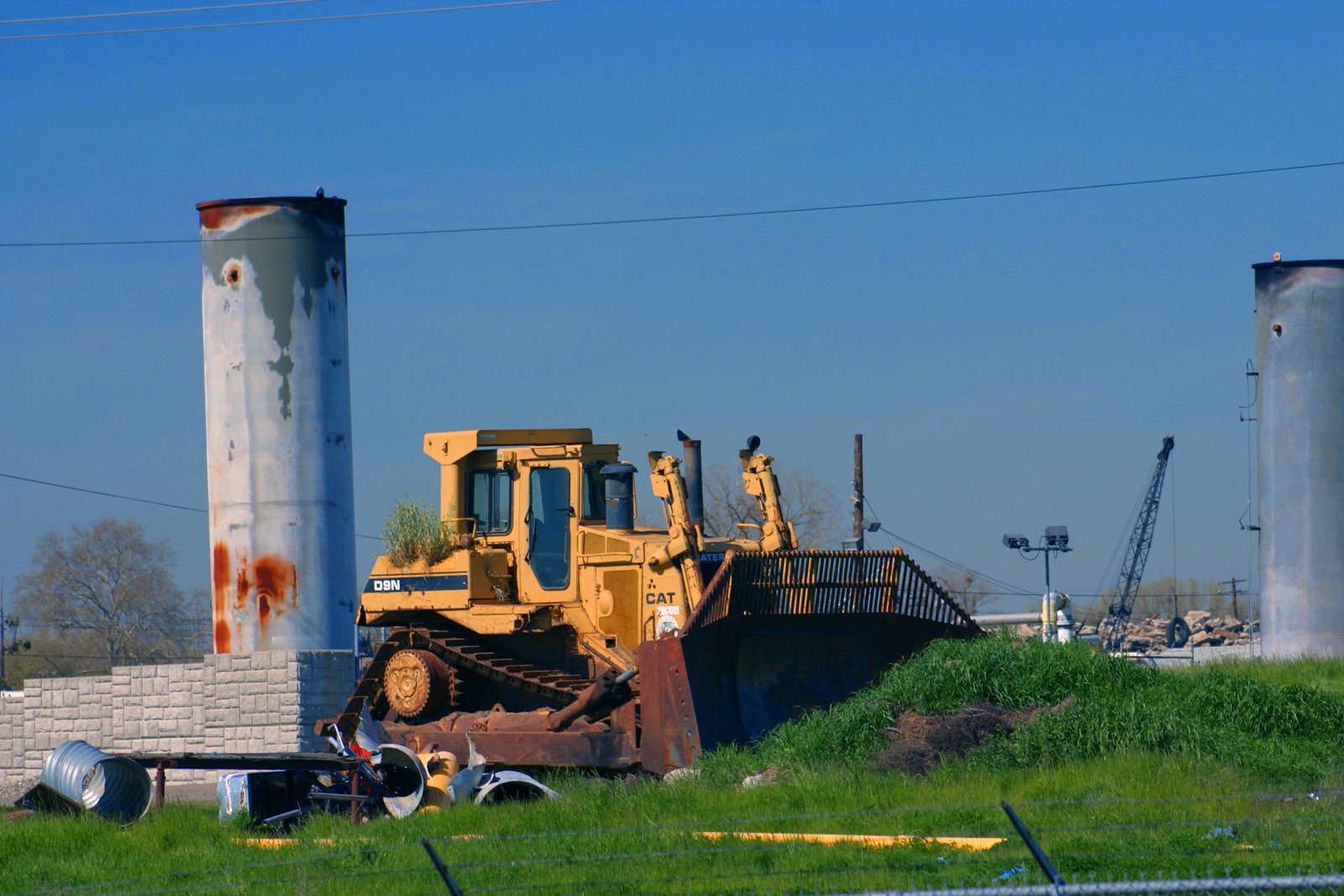 a bulldozer with the back wheels extended sits next to a cement silo