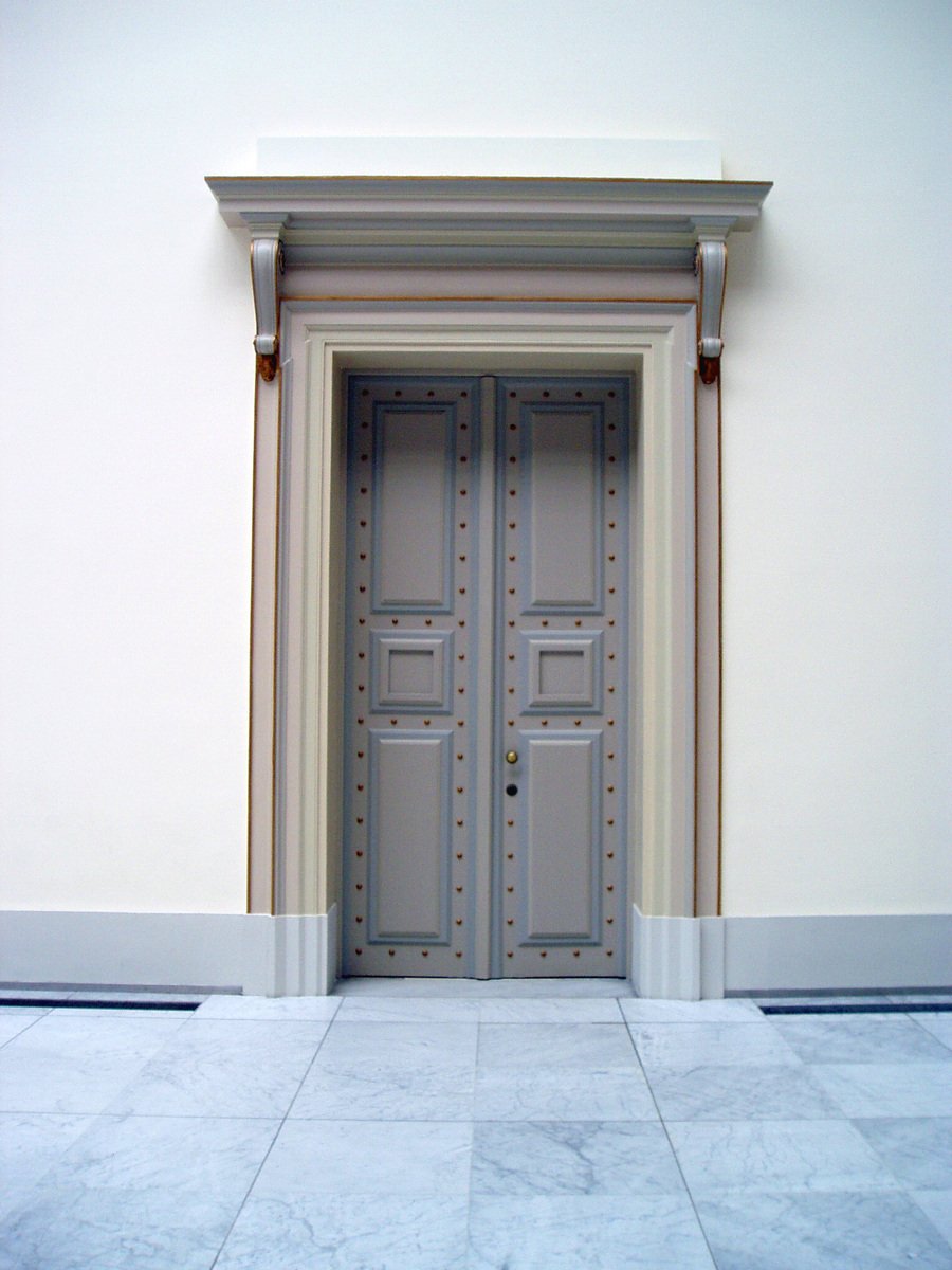 a beige and gray door a white wall and a stone floor