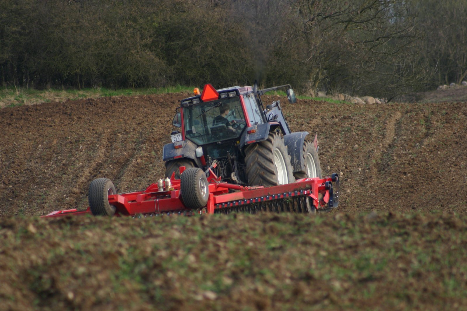 a tractor working in the field with trees behind