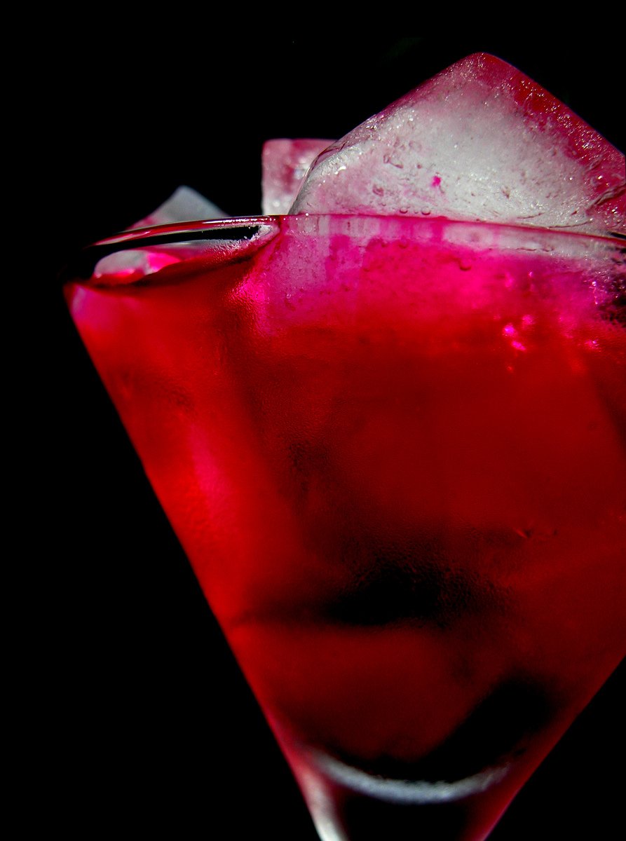 a red drink with ice sitting in a dark place