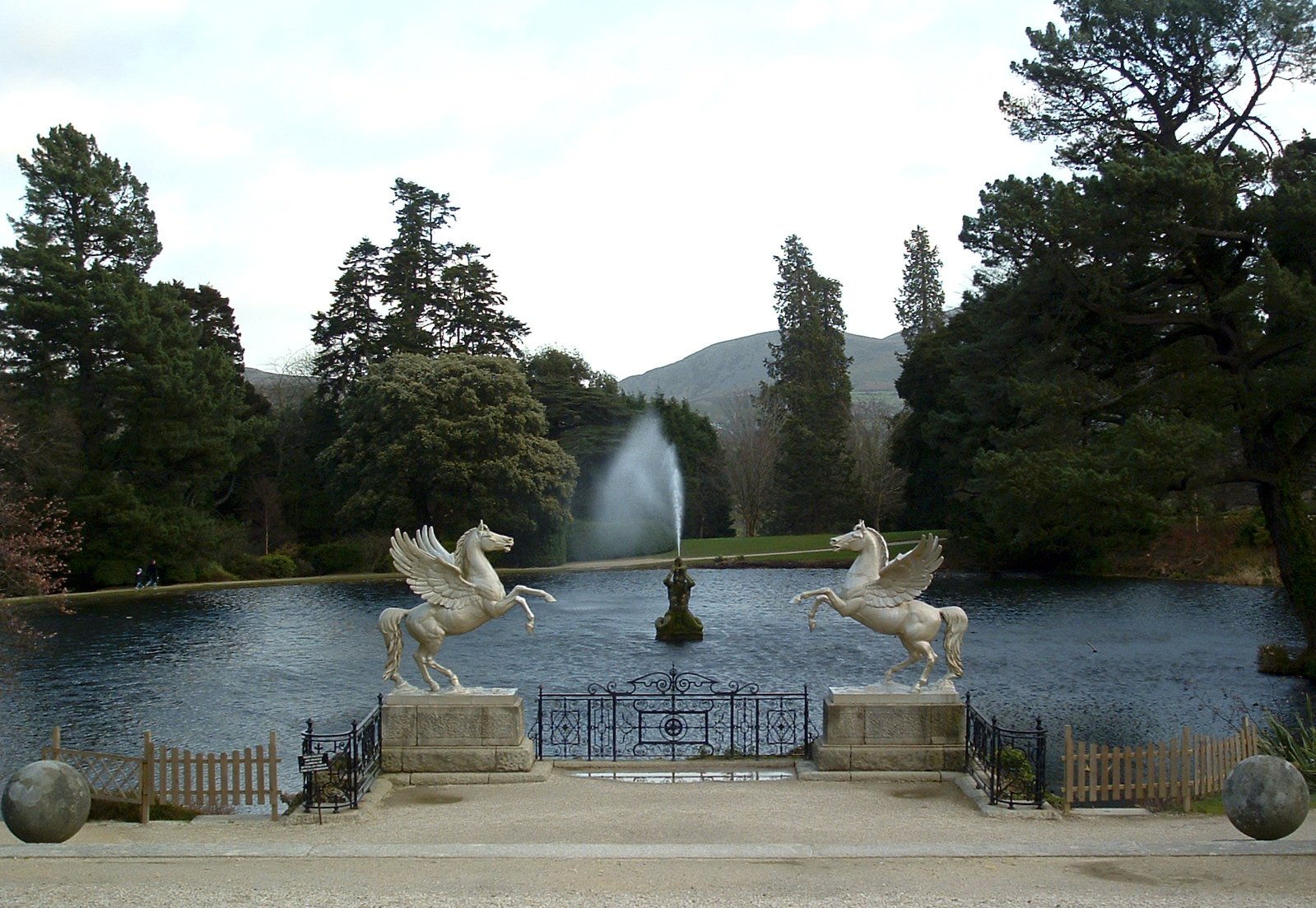 a pond that has two statues of horses and fountains