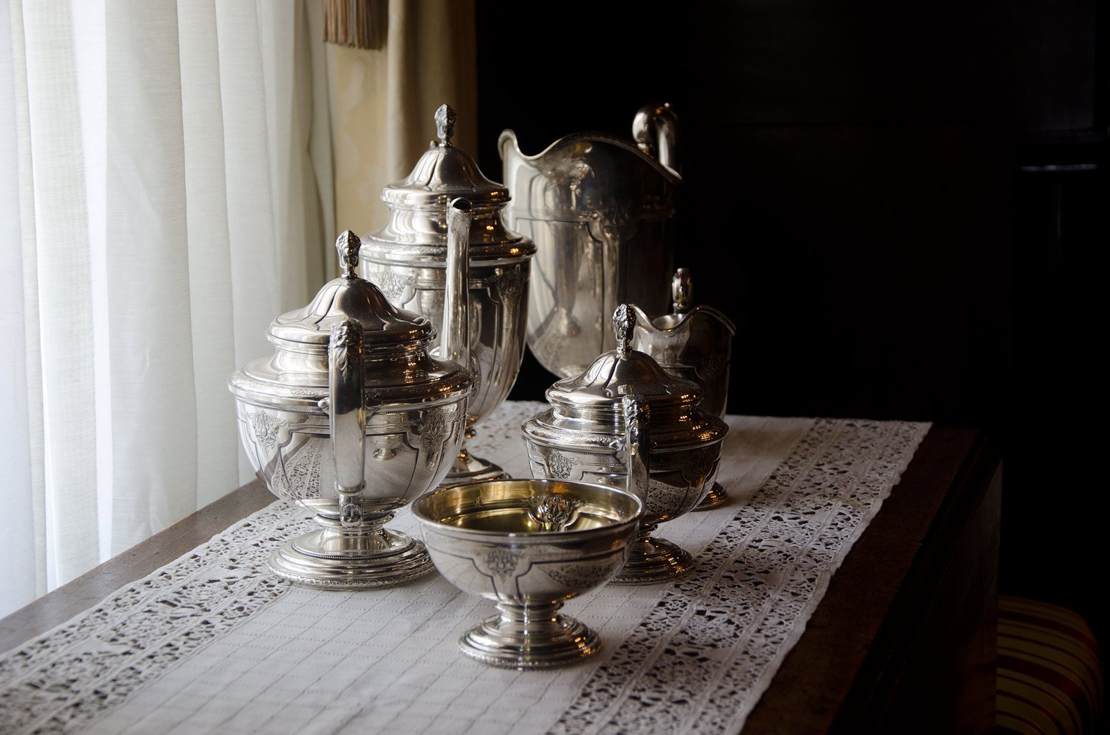a silver bowl is on top of a lace table cloth