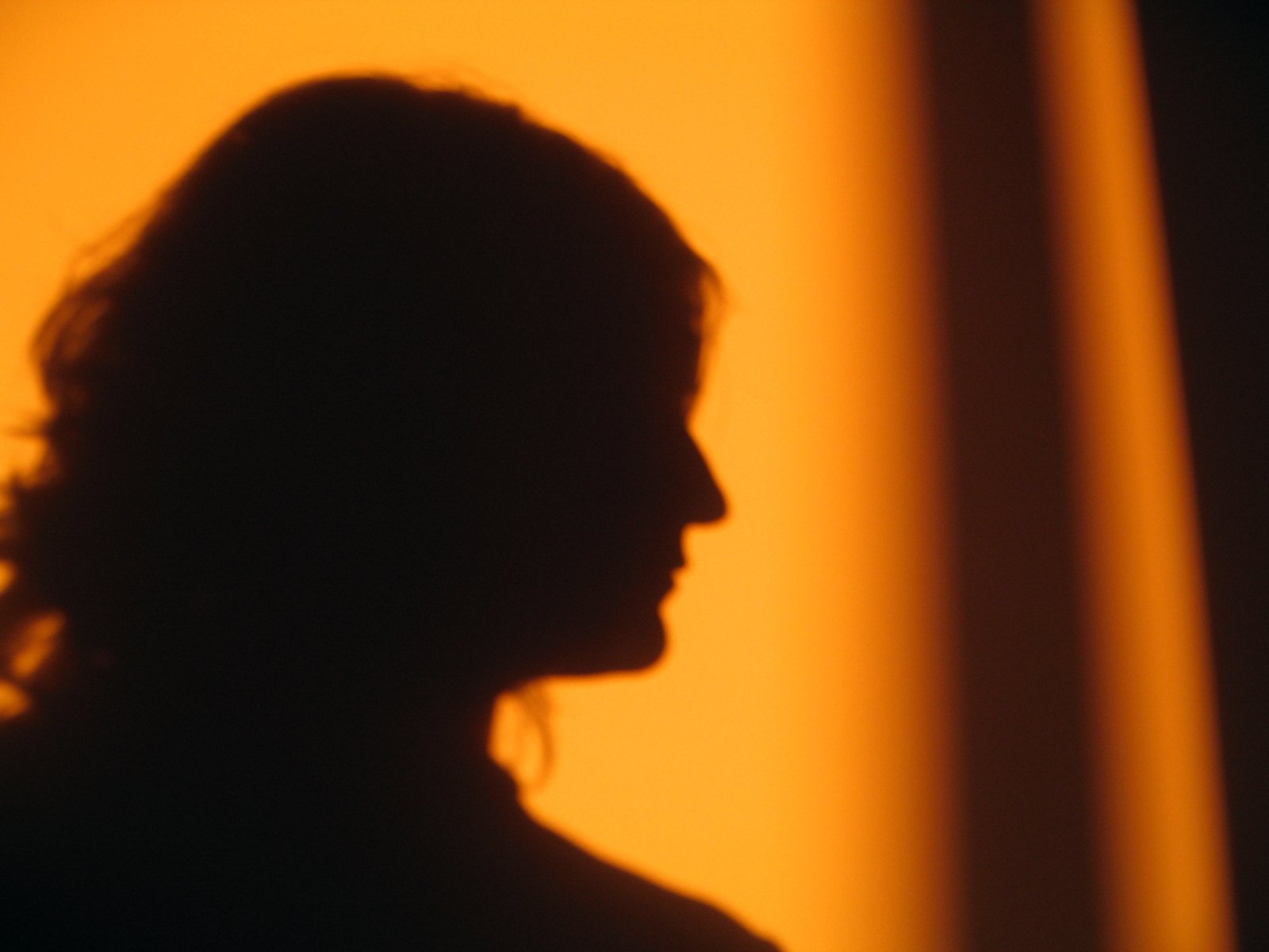 the silhouette of a woman standing against a yellow wall