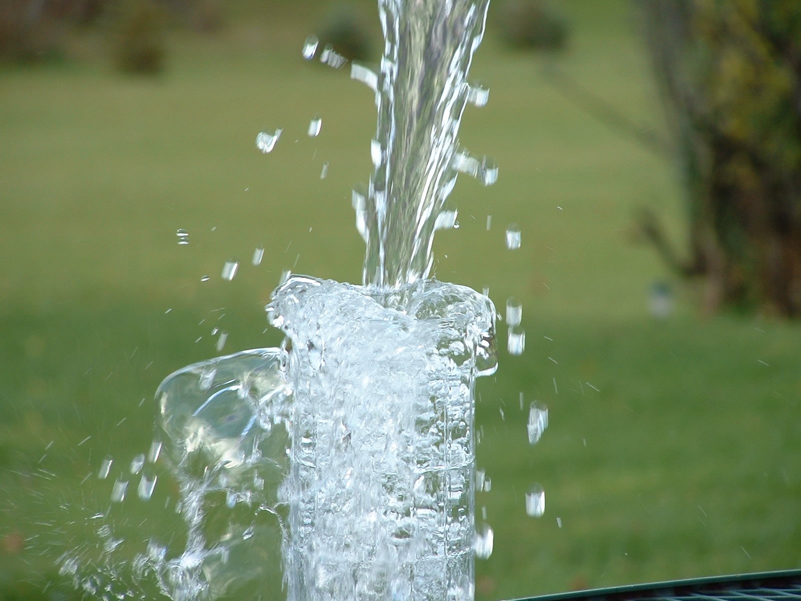 water is pouring out of the top of a tall glass