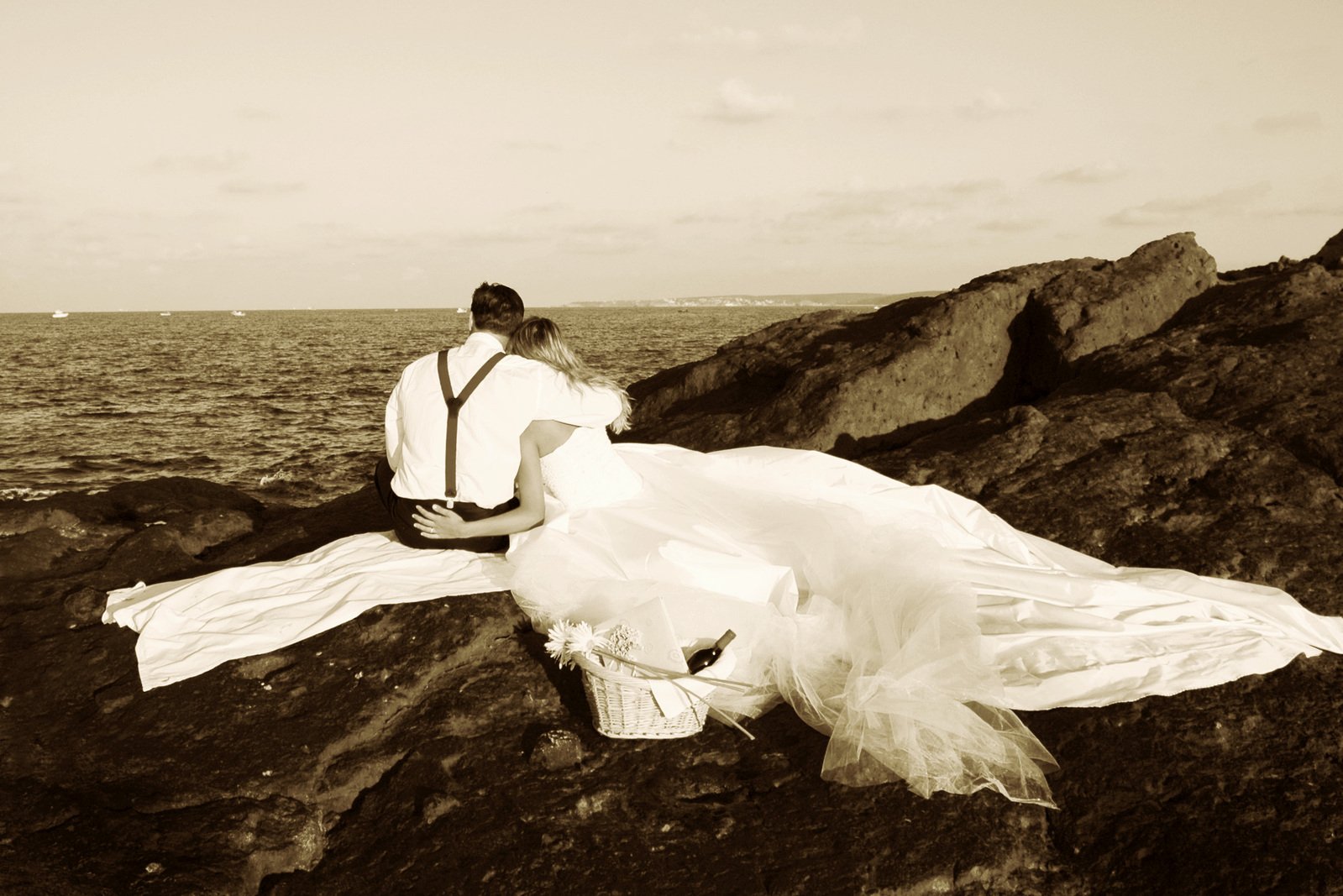 a couple is sitting on a rock with the ocean in the background
