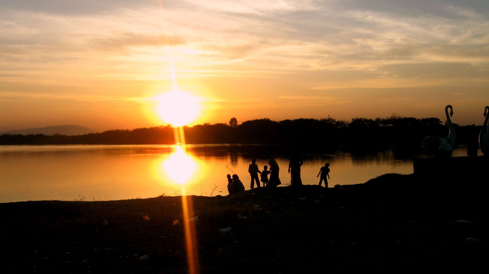 the sun is setting over a lake as people walk near
