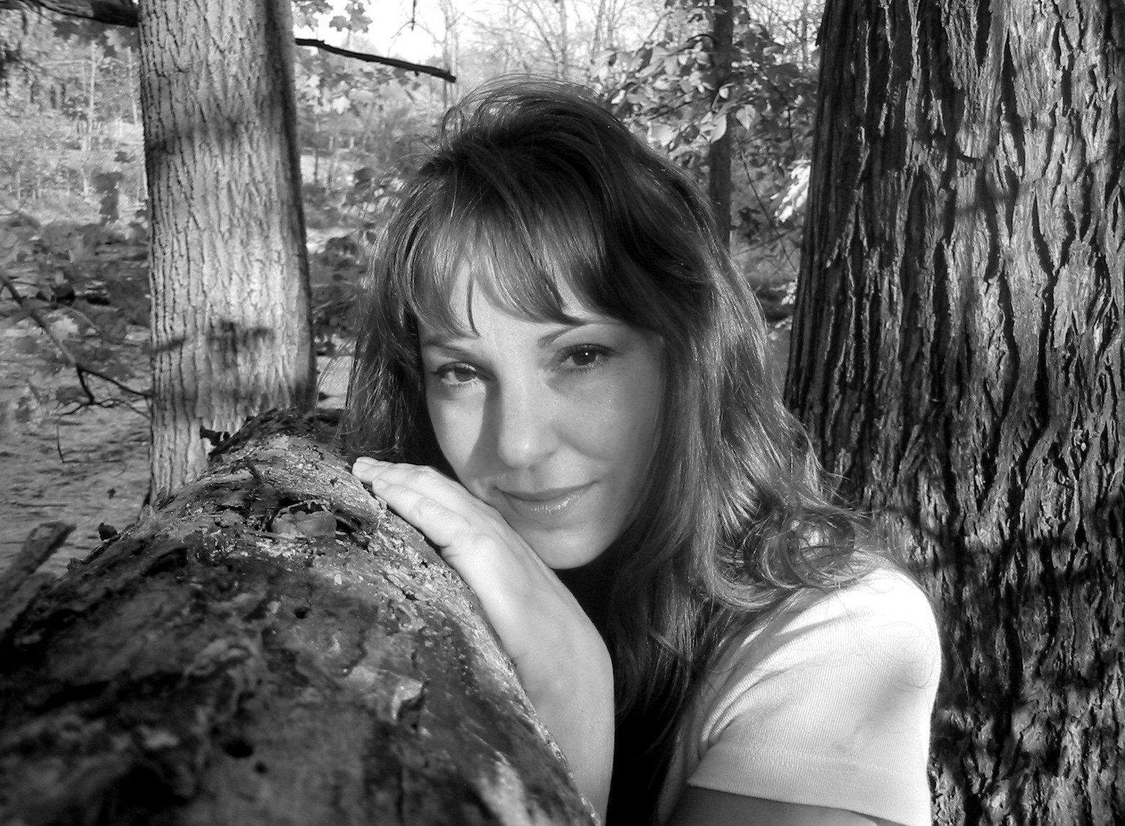 a woman standing by a large tree leaning her head against the trunk