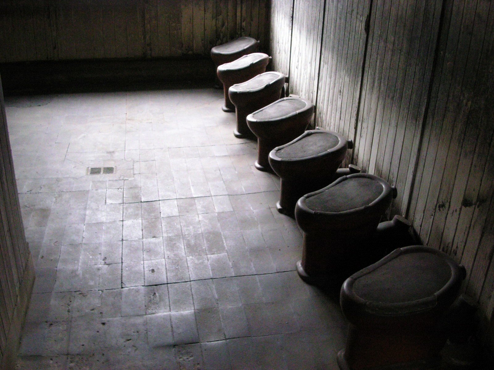 six urinals line a wall in a dimly lit bathroom