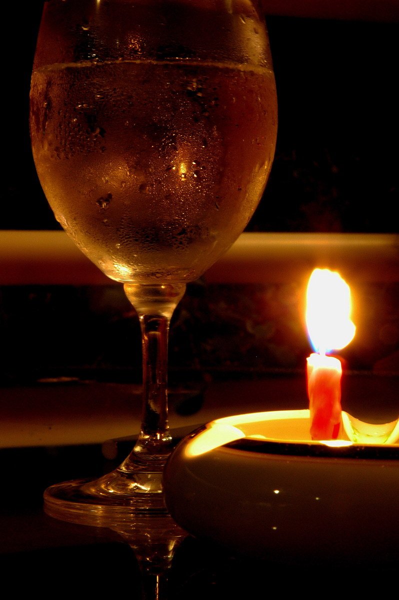 a small lit candle in front of an empty wine glass