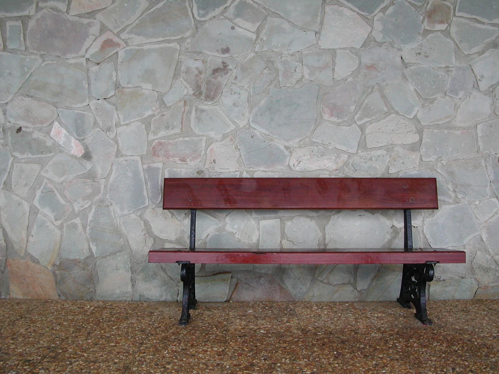 a long wooden bench sitting next to a stone wall