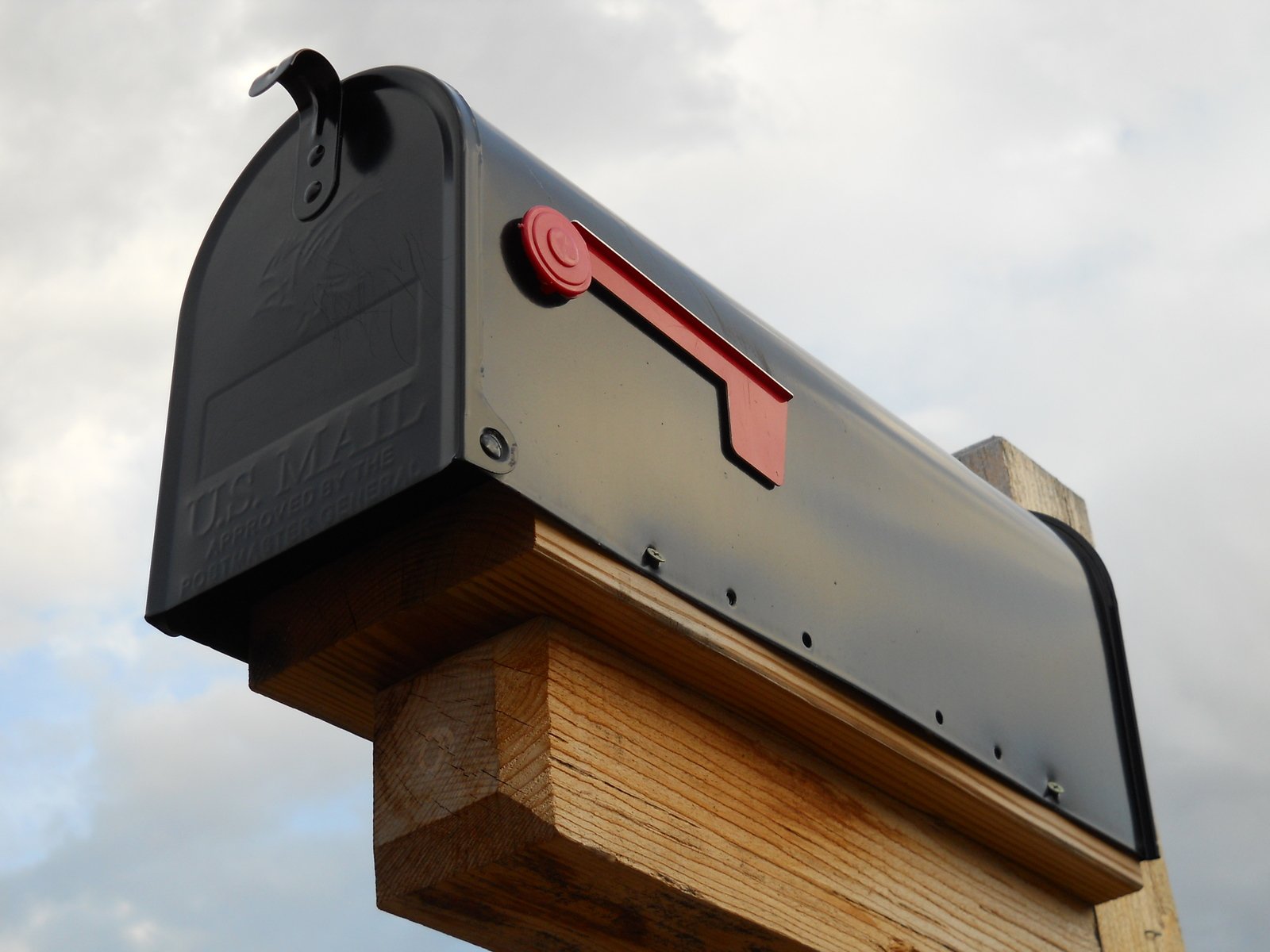 a black mailbox sits near a tree and clouds