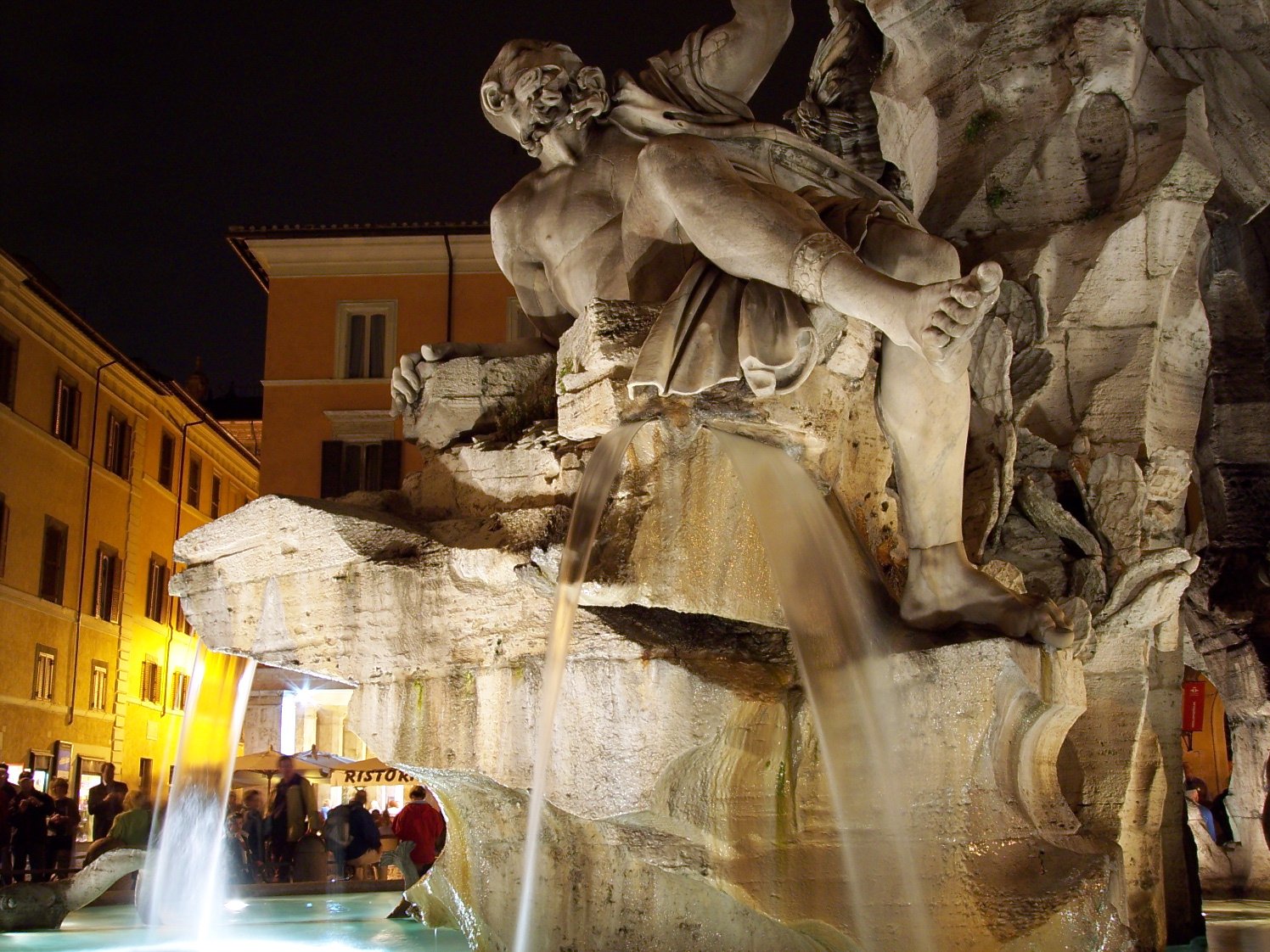 a fountain with a statue of a man holding a sword is surrounded by people standing in the background