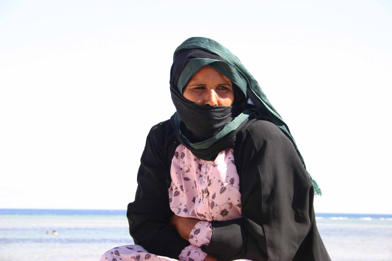 a woman is sitting on the sand looking out into the ocean