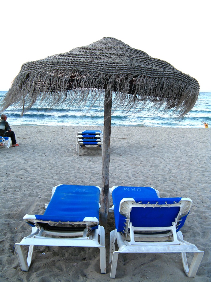 two lawn chairs and an umbrella are sitting on the beach