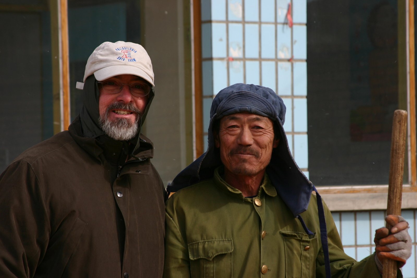 two men in winter clothes, one is holding a baseball bat