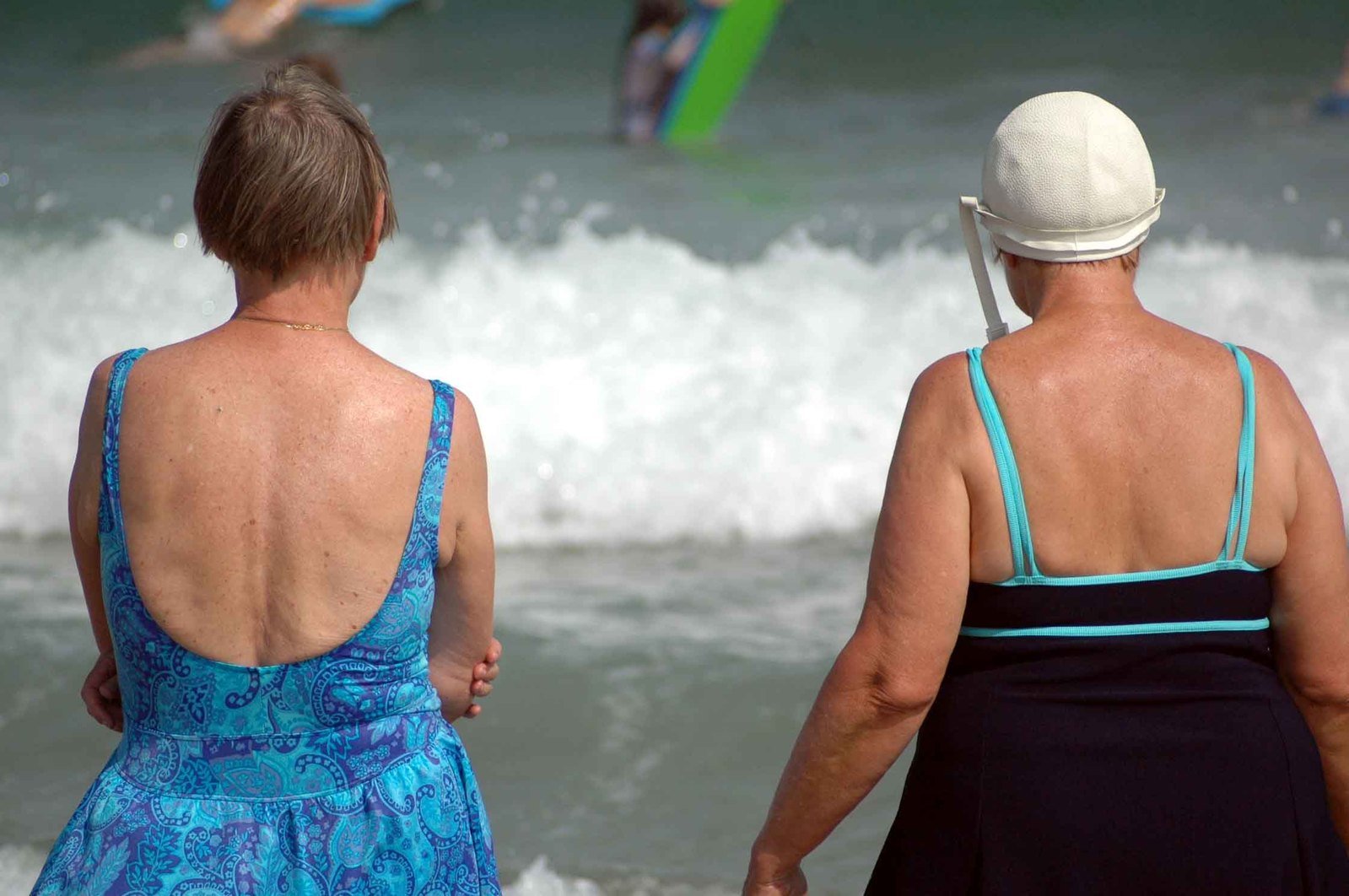 two women standing in the ocean on the beach with people playing in the waves