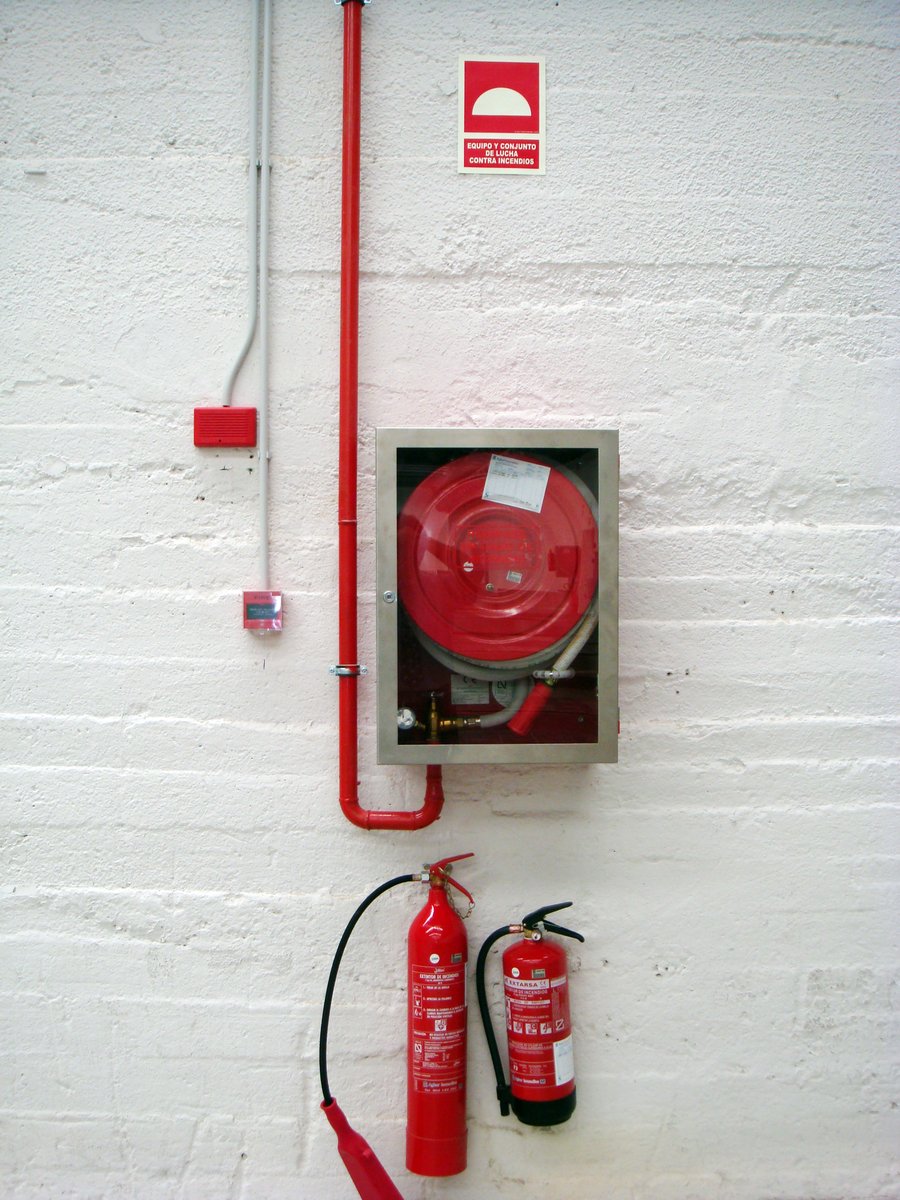 a wall with two fire hydrants, an emergency switch and two hoses