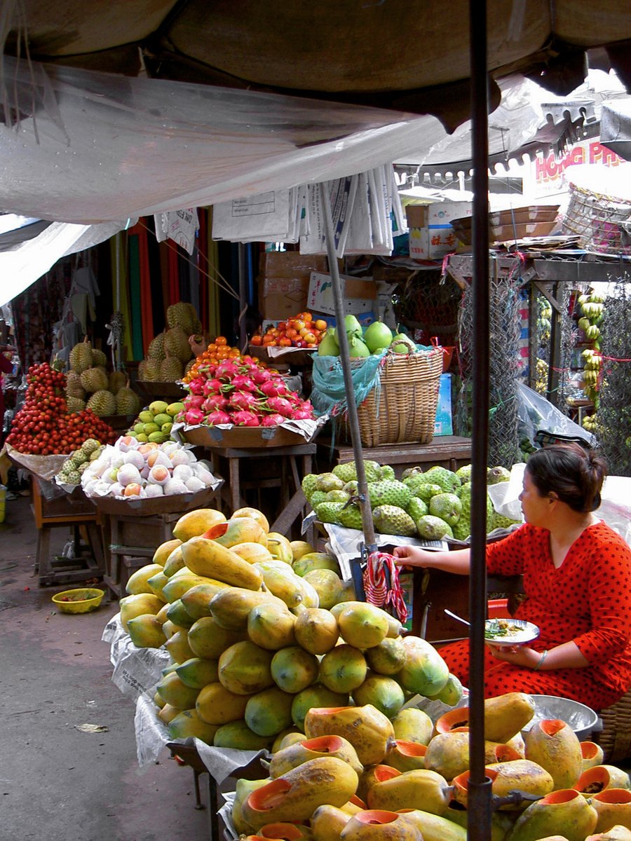 an outdoor market has bananas, oranges, and other produce