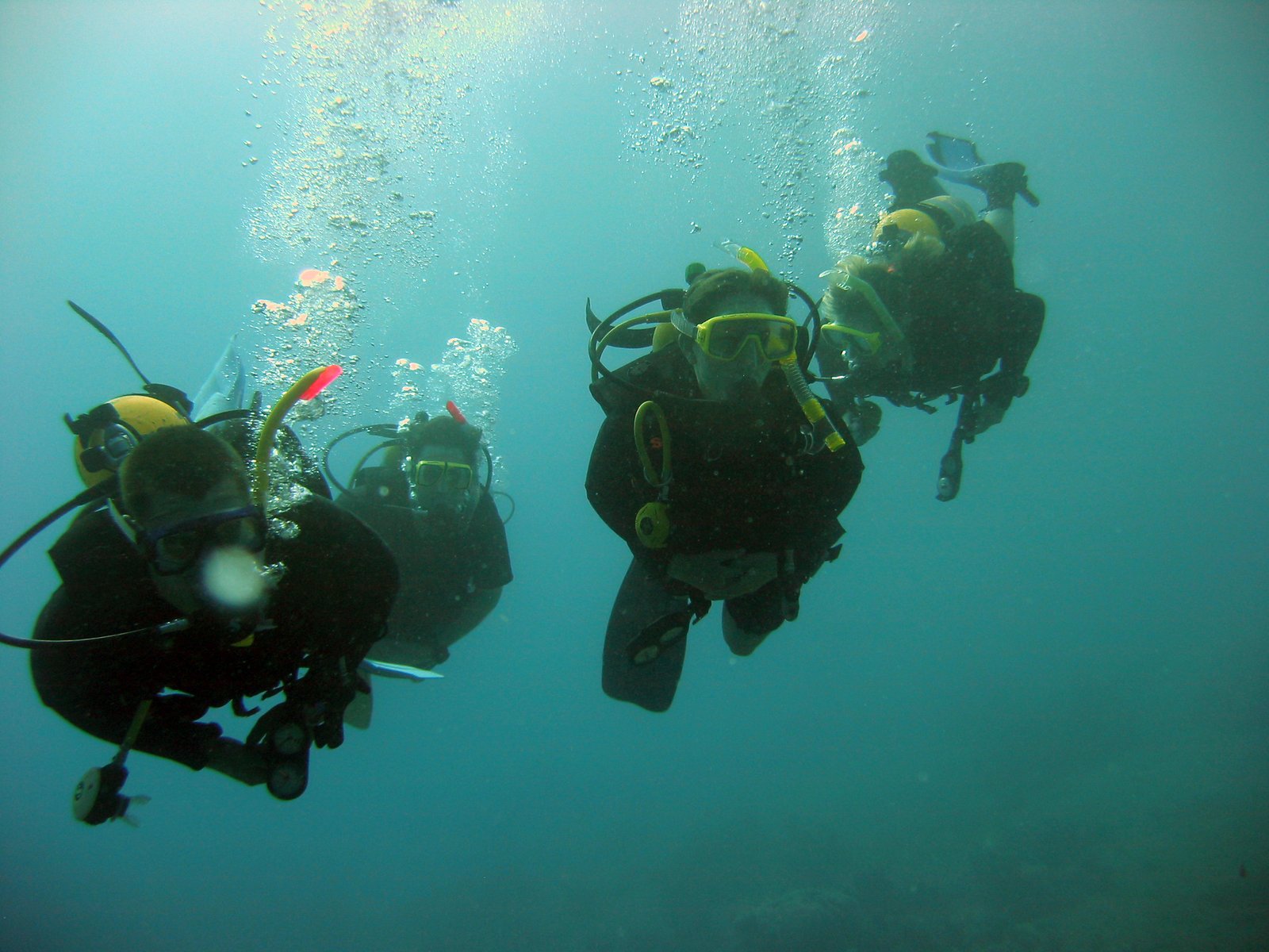 three scuba divers take off in clear blue water