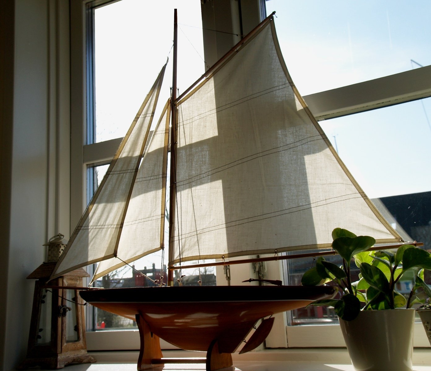 a toy model sailboat sitting on top of a tray next to potted plants