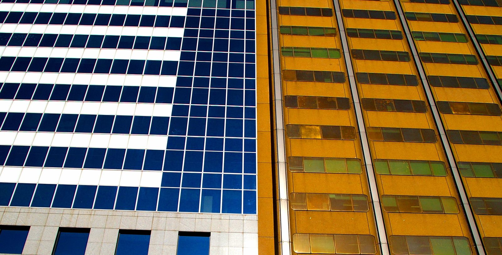 two modern buildings with glass windows and yellow one with green