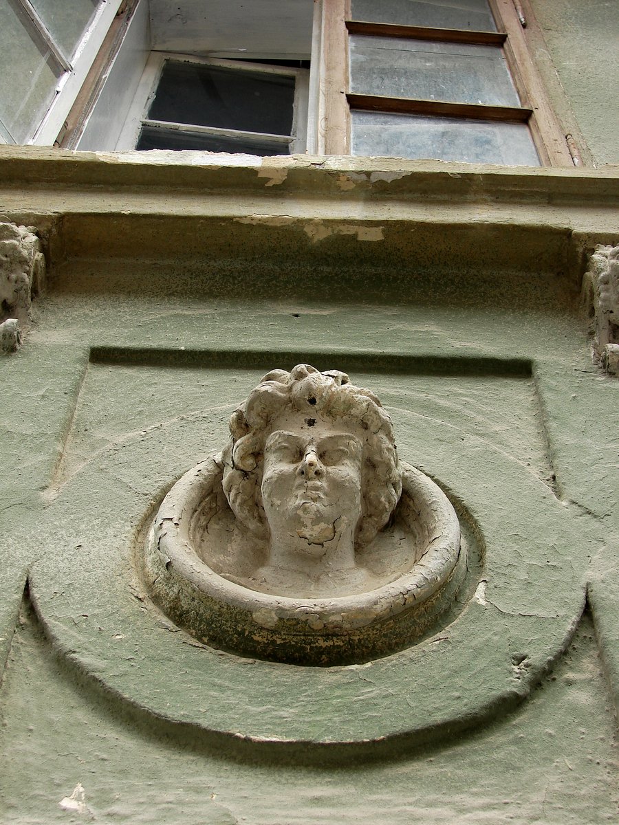 the stone head of a stone lion decorates the corner of an old building