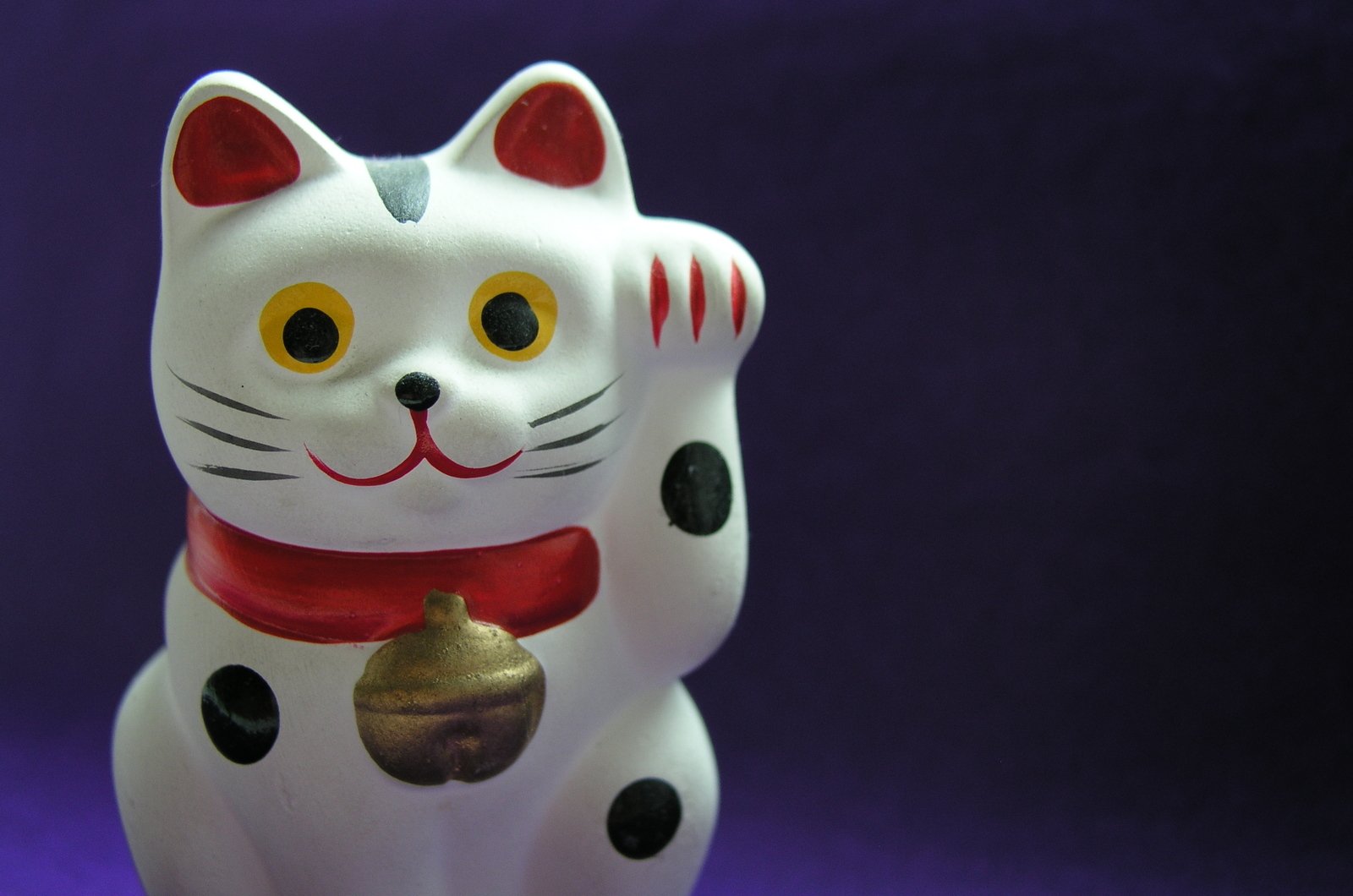 a white cat figurine is wearing a red scarf and a bell
