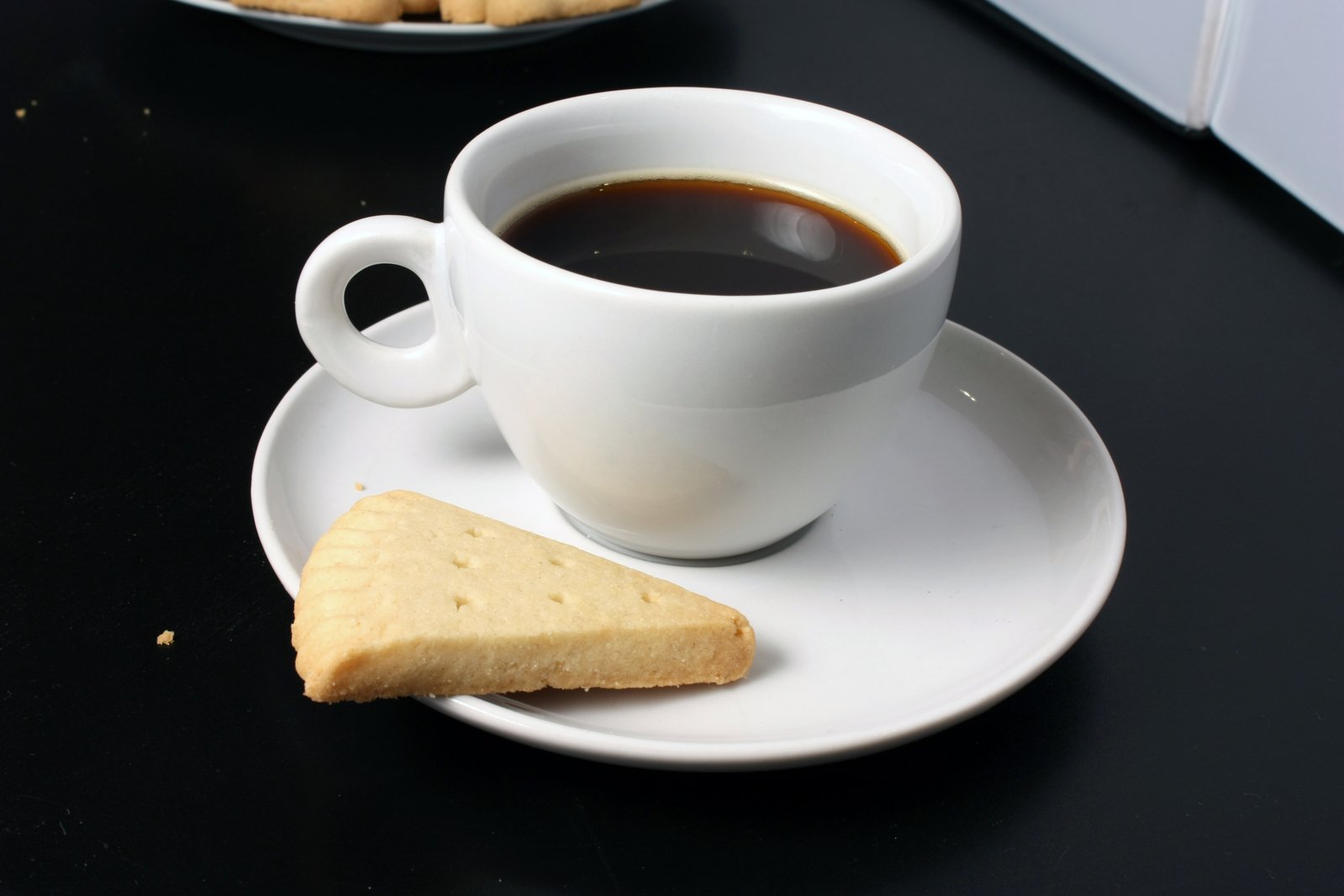 a cup of coffee next to a piece of cookies on a plate