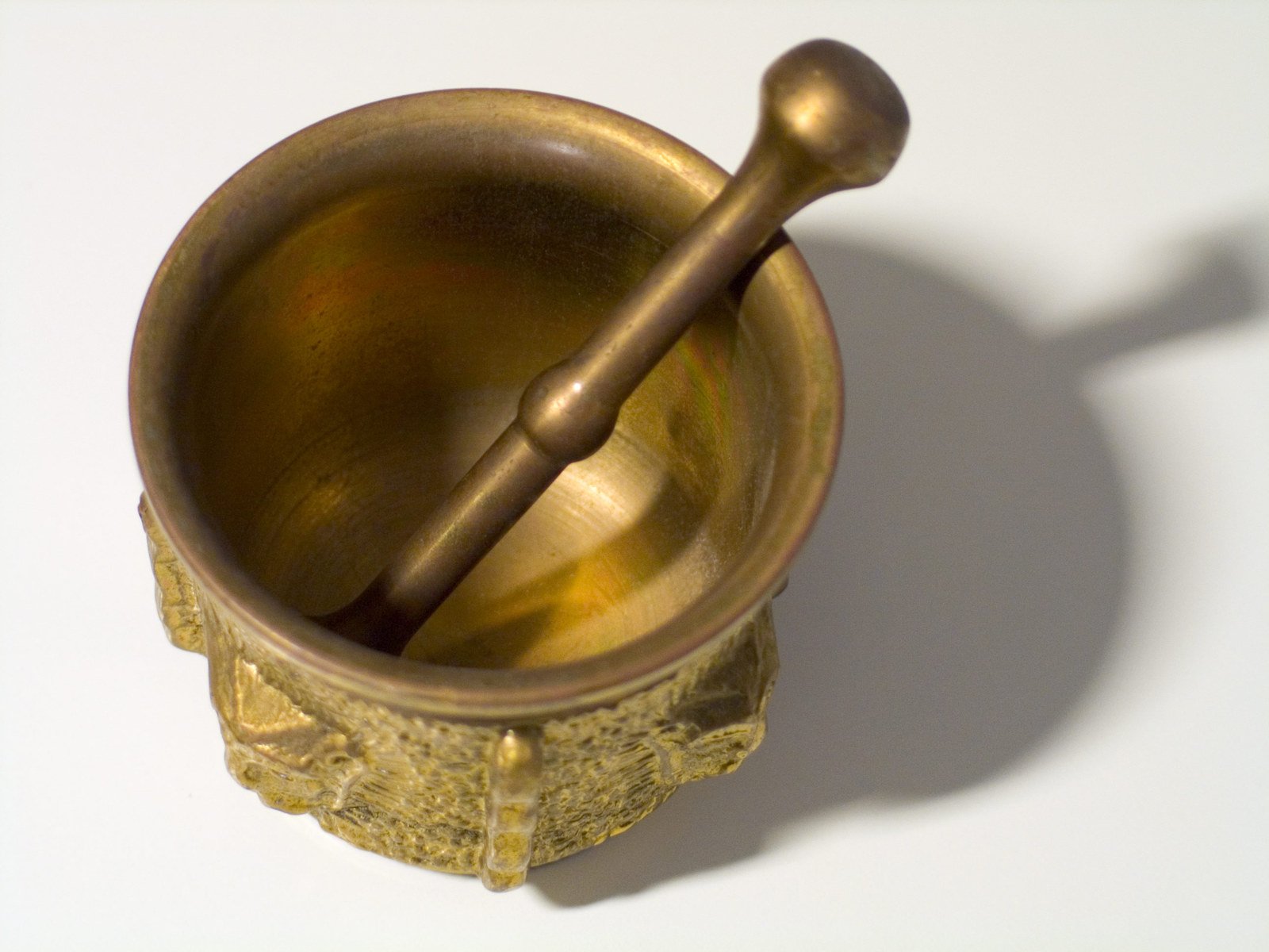 a gold bowl and two spoons, on a white surface