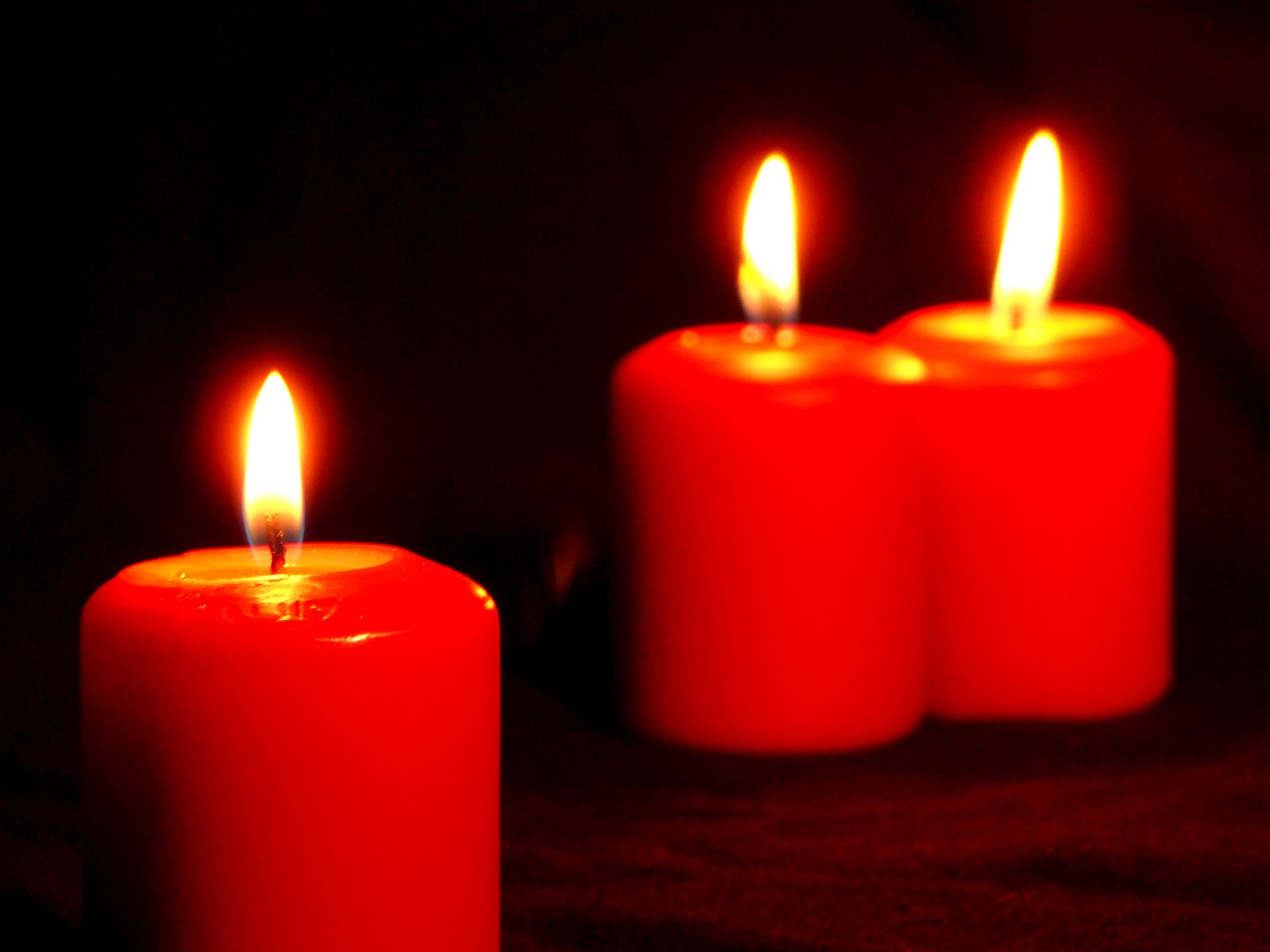 three red candles with a black background