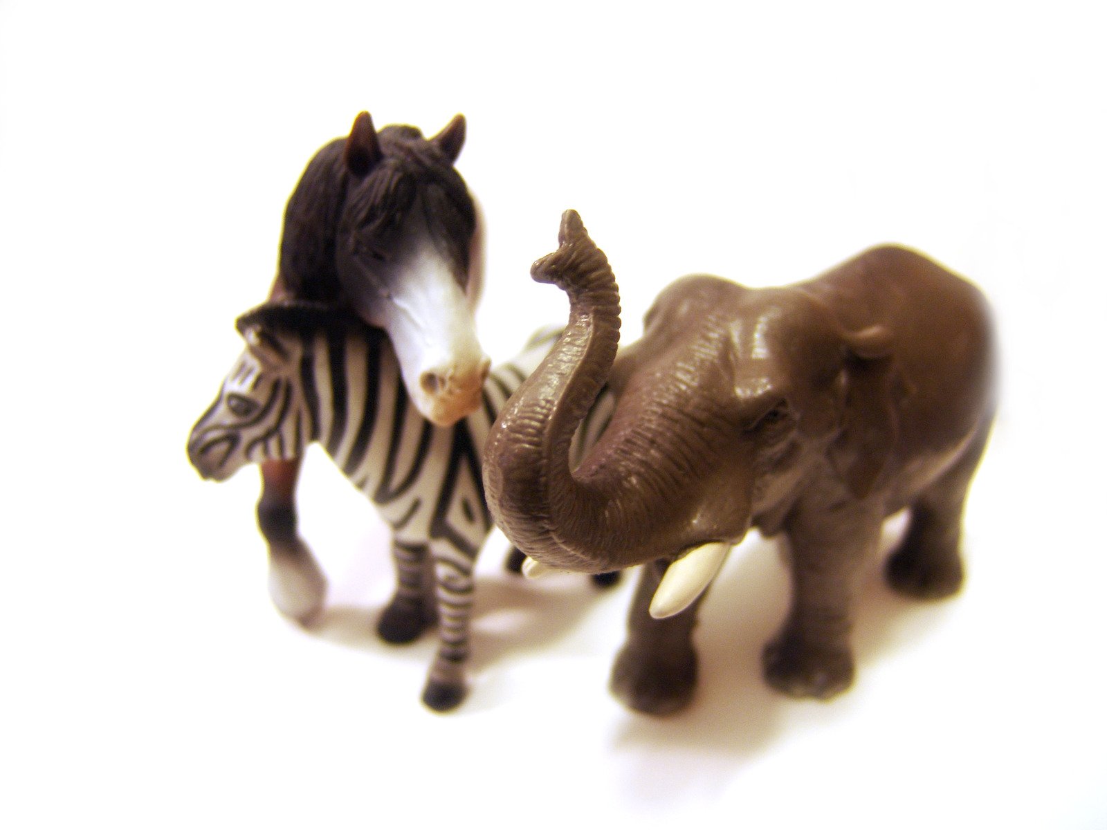 two plastic elephants and one elephant that has a striped tail