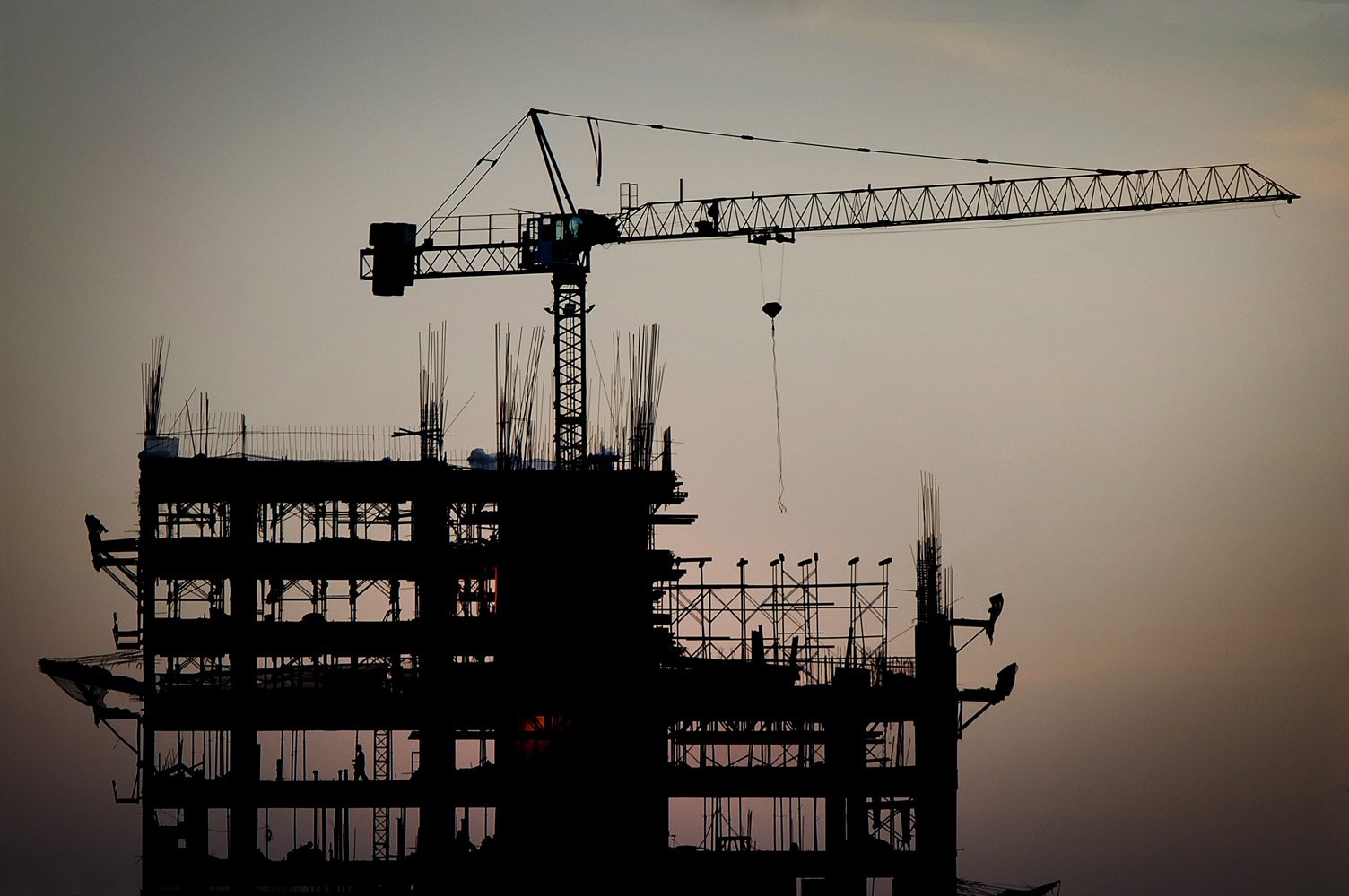 silhouette of a large crane with buildings under construction