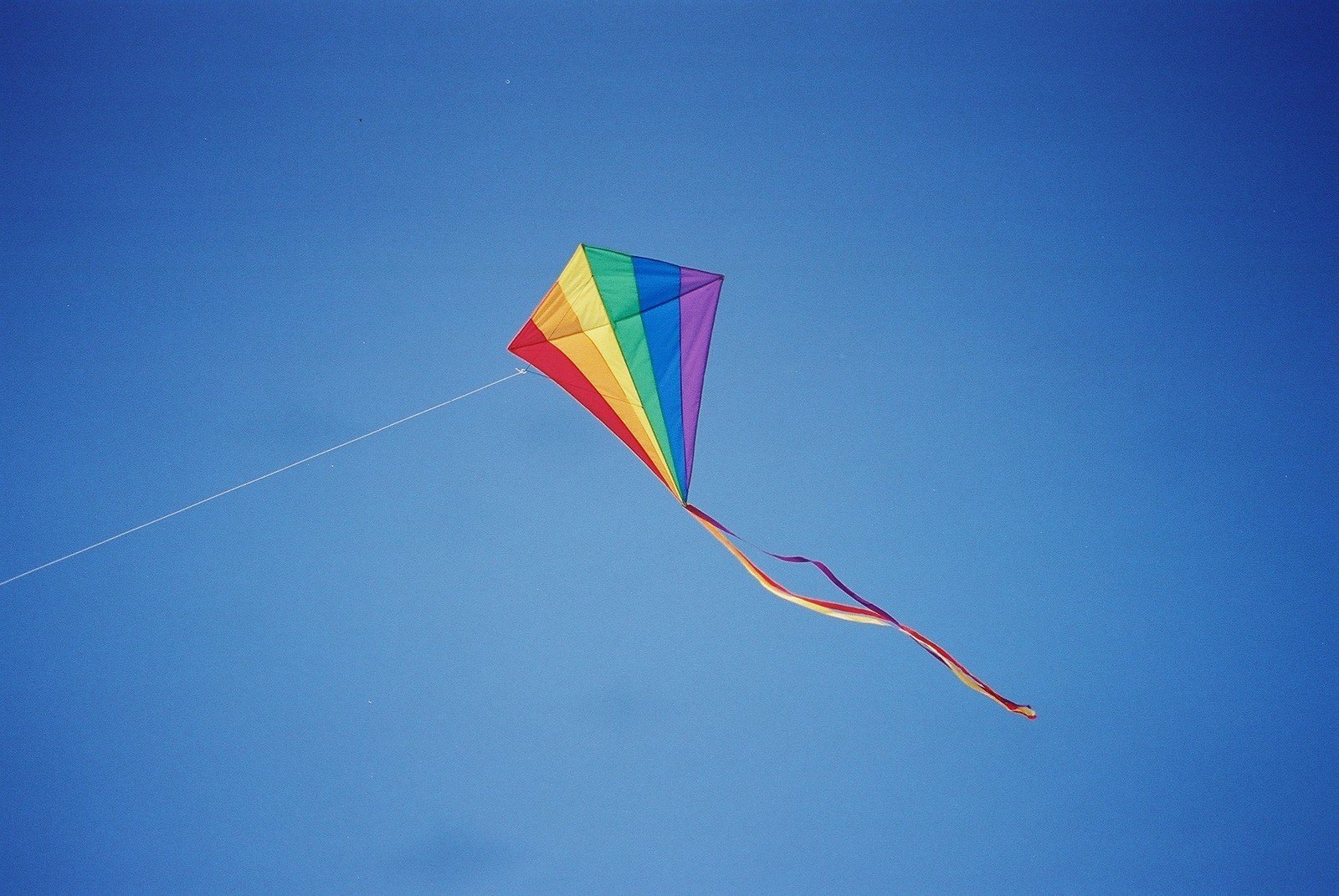 a rainbow kite is in the blue sky