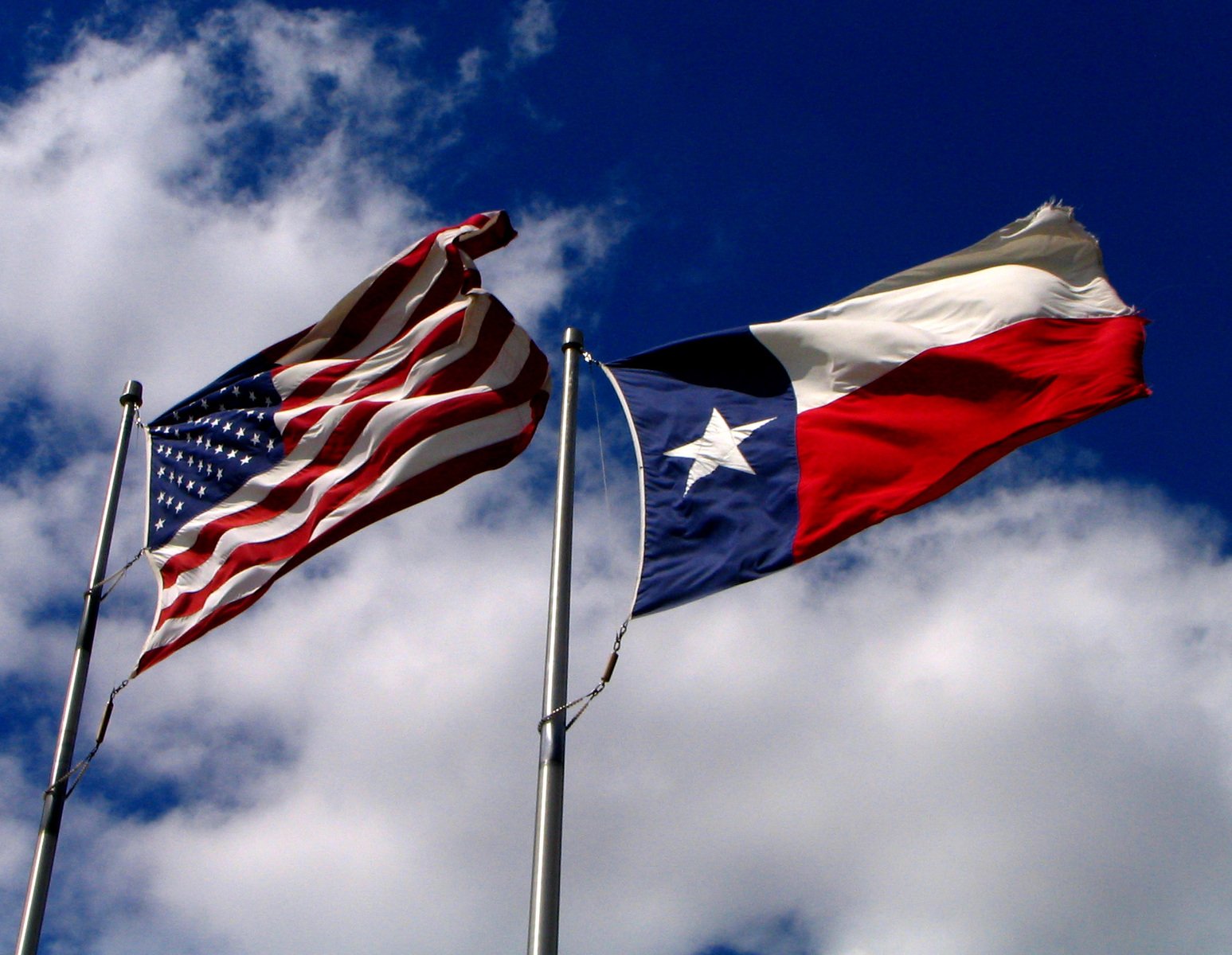 two american and texas flags flying in the blue sky