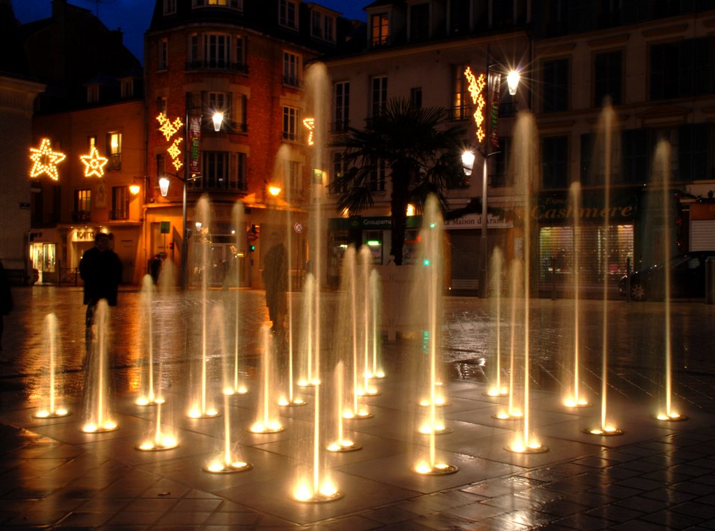 illuminated fountains on a brick floor next to city buildings