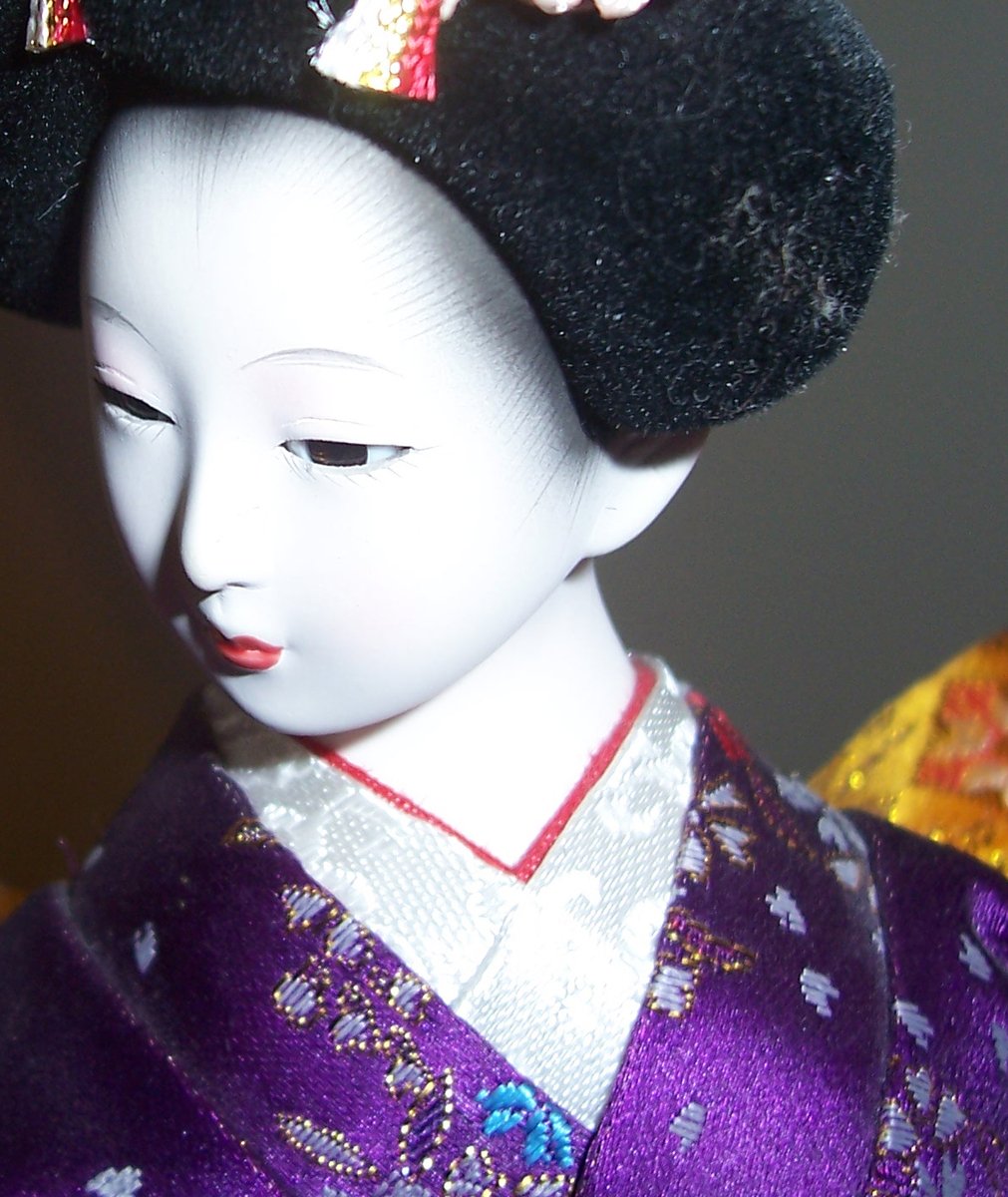 a geisha doll wearing a black hat with flowers