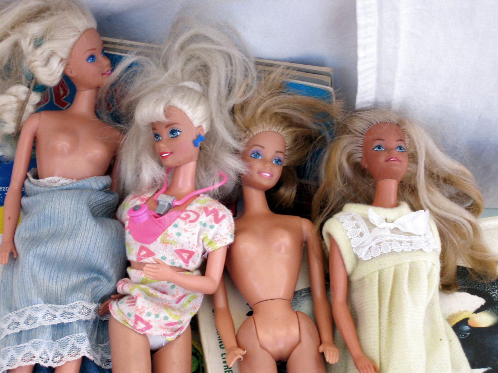 four dolls are on a bed and one is wearing pajamas