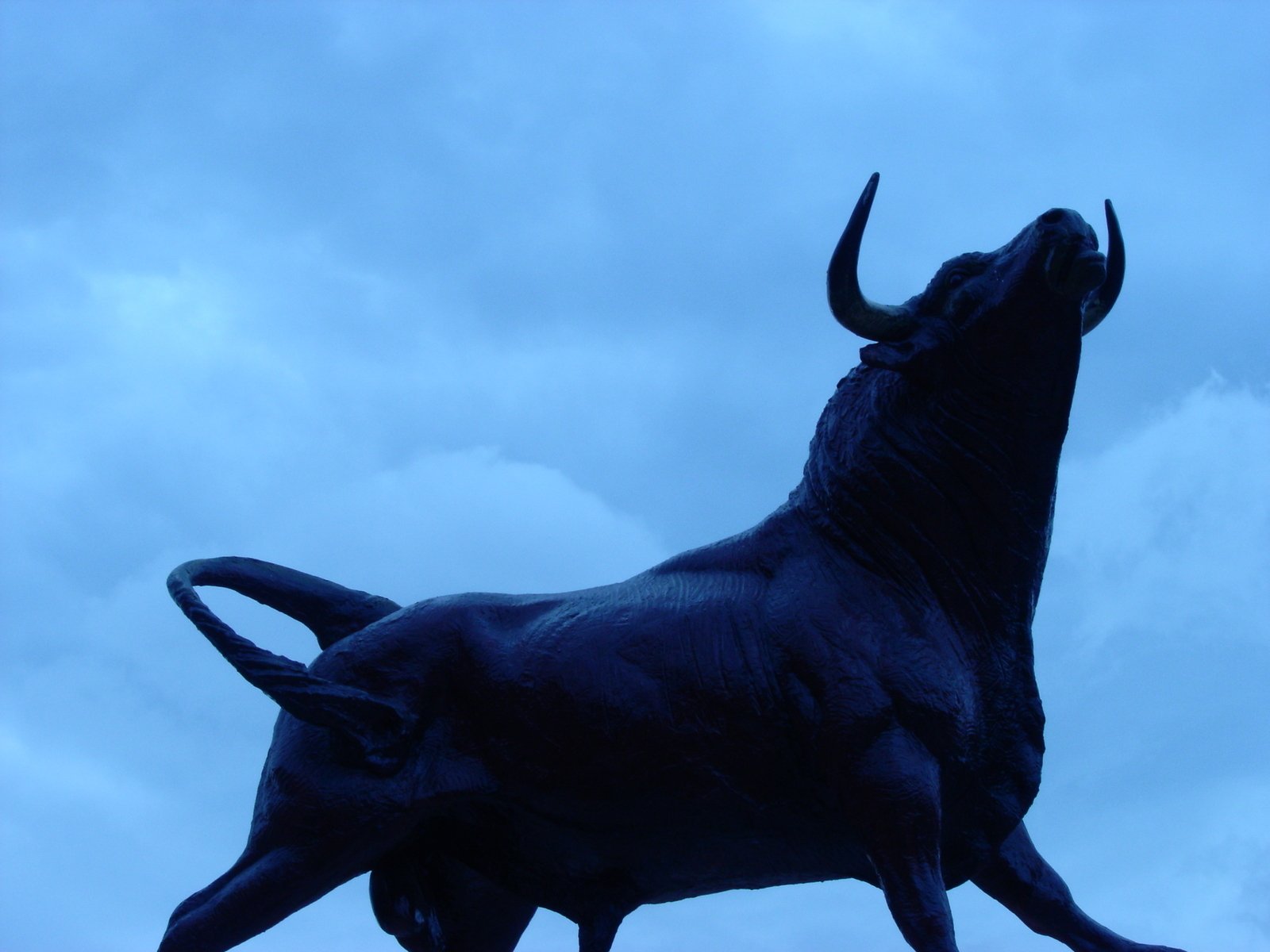 a statue of a bull in front of a cloudy sky