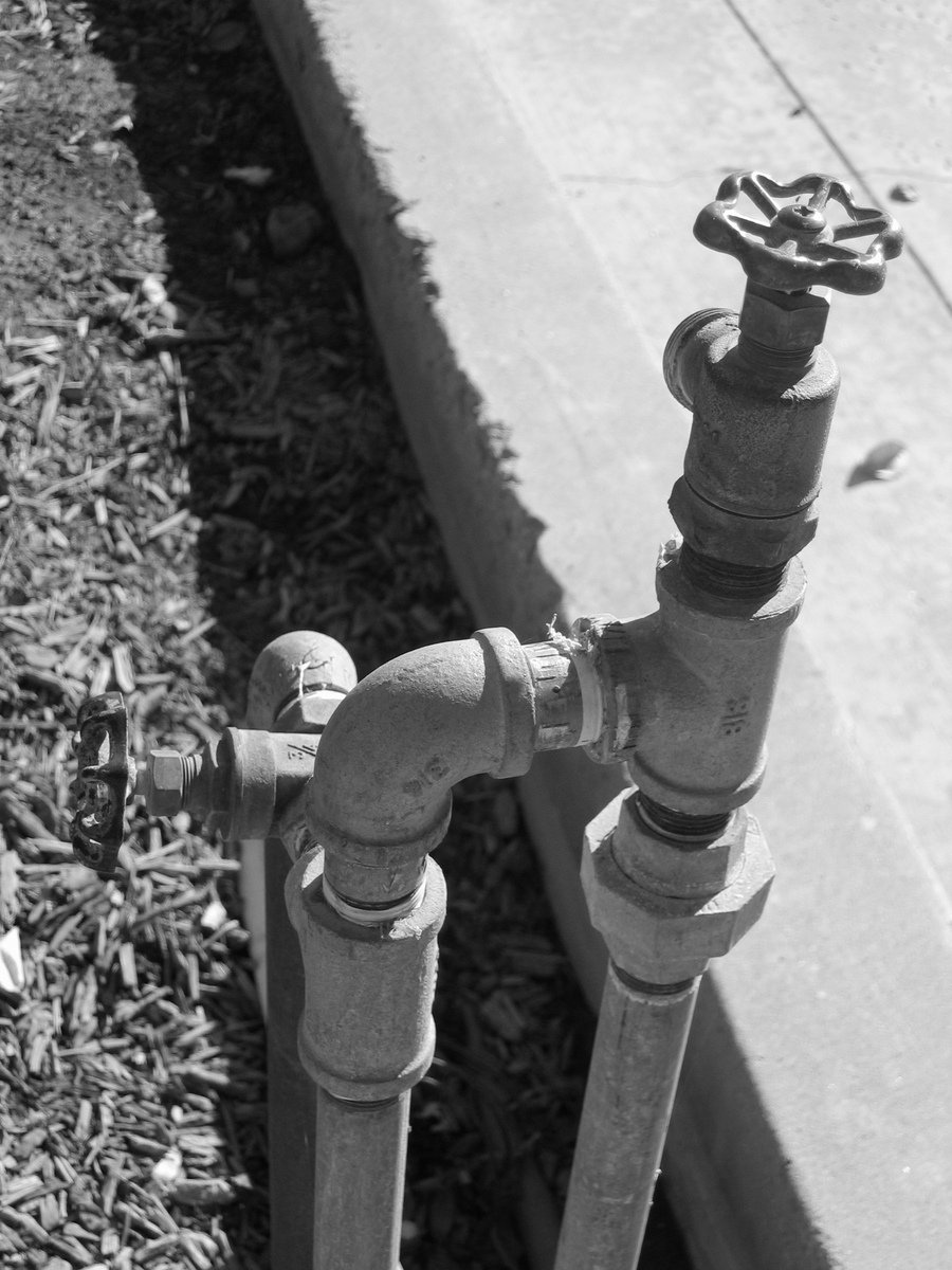 a black and white picture of an old spigot next to a concrete walkway