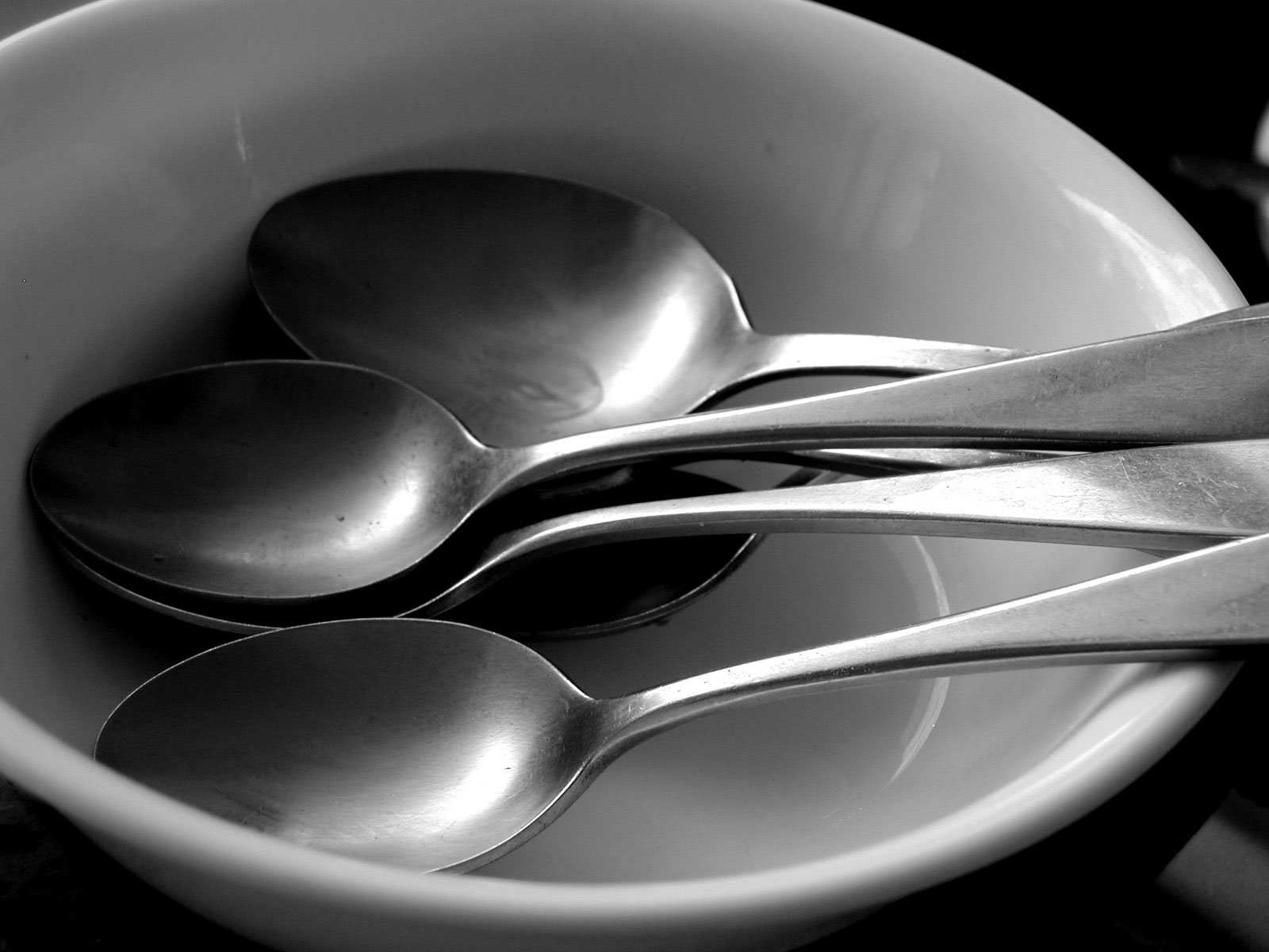 a white bowl holding four silver spoons in it
