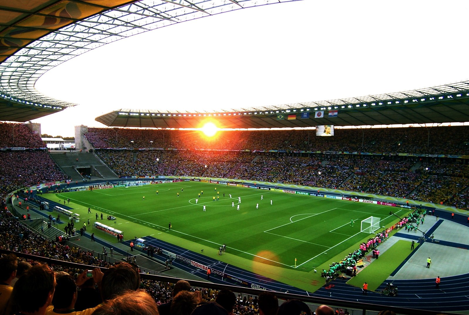 a soccer stadium with a green field and the sun setting on the horizon