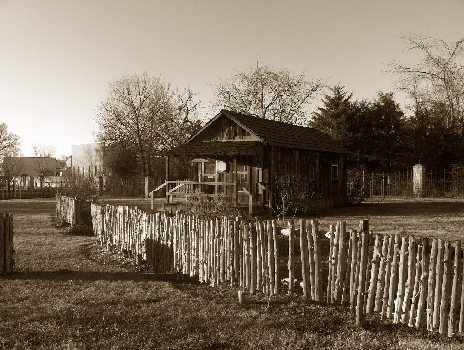 the old wooden house stands by a fence and some trees