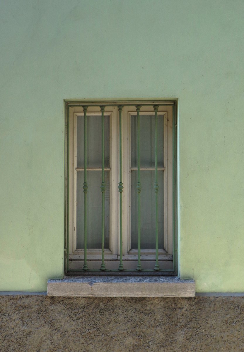 a window in the side of a green wall with a metal door