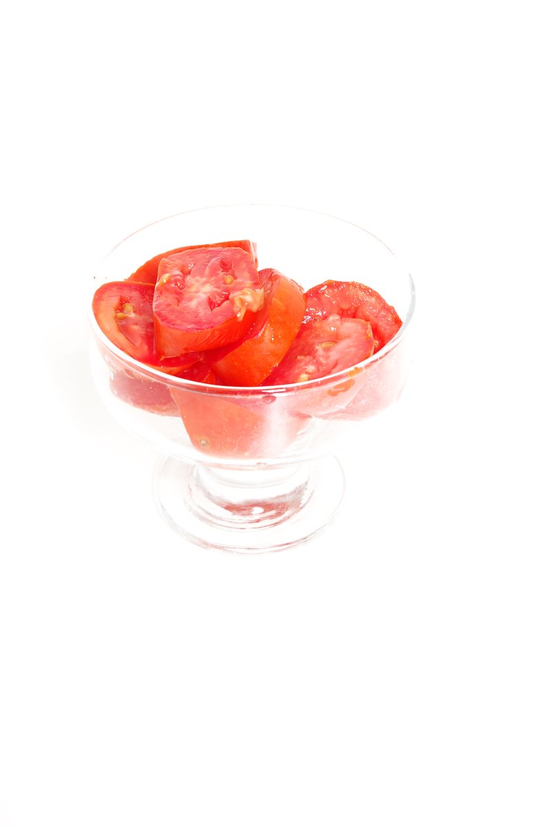 a glass bowl filled with sliced tomatoes on top of a white table