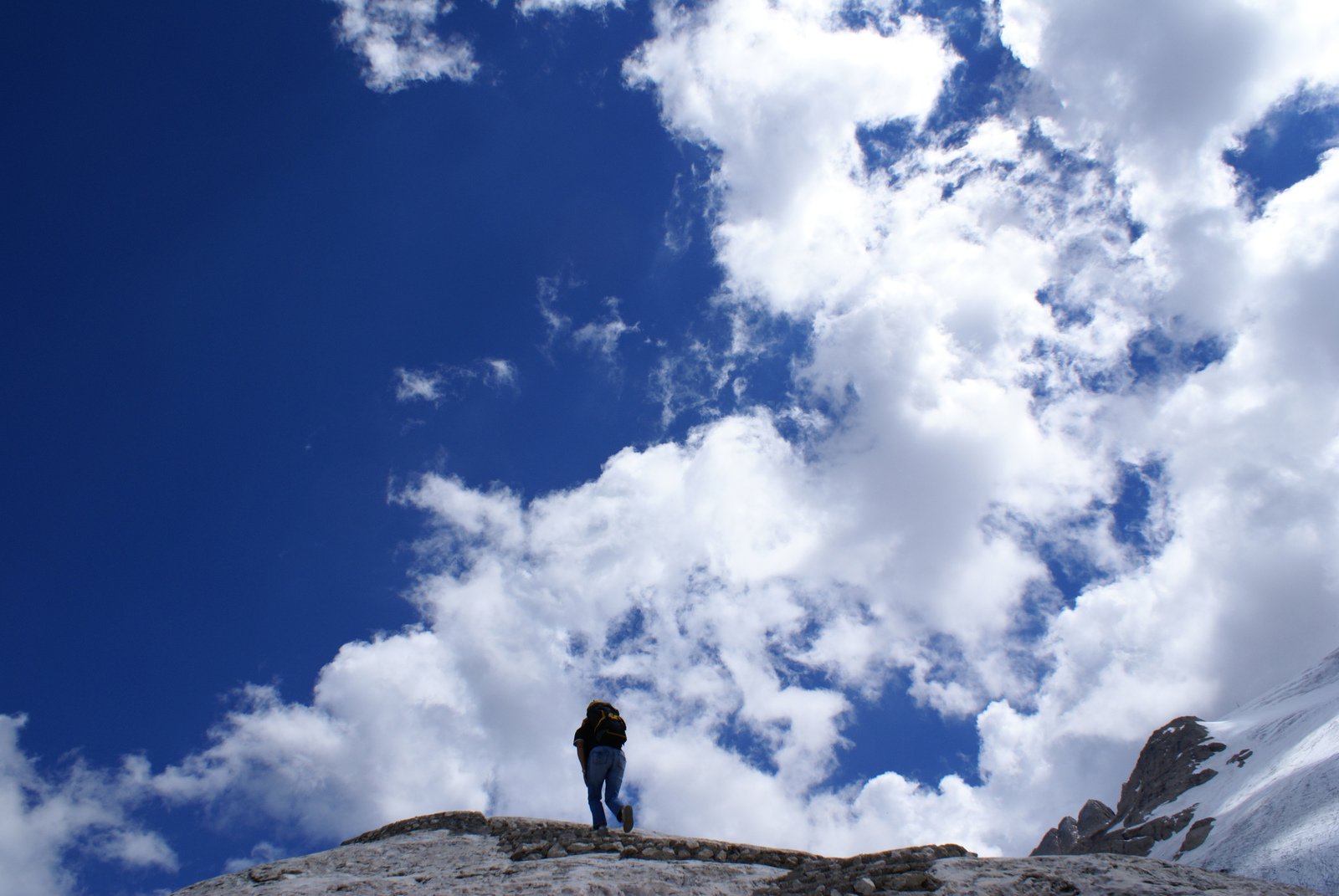 man standing on a rocky ledge gazing at mountains under a cloudy sky