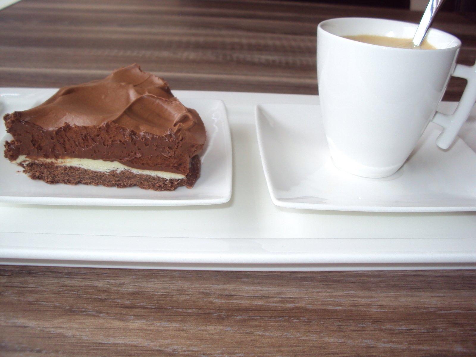 a piece of chocolate dessert on a white plate next to a cup of coffee